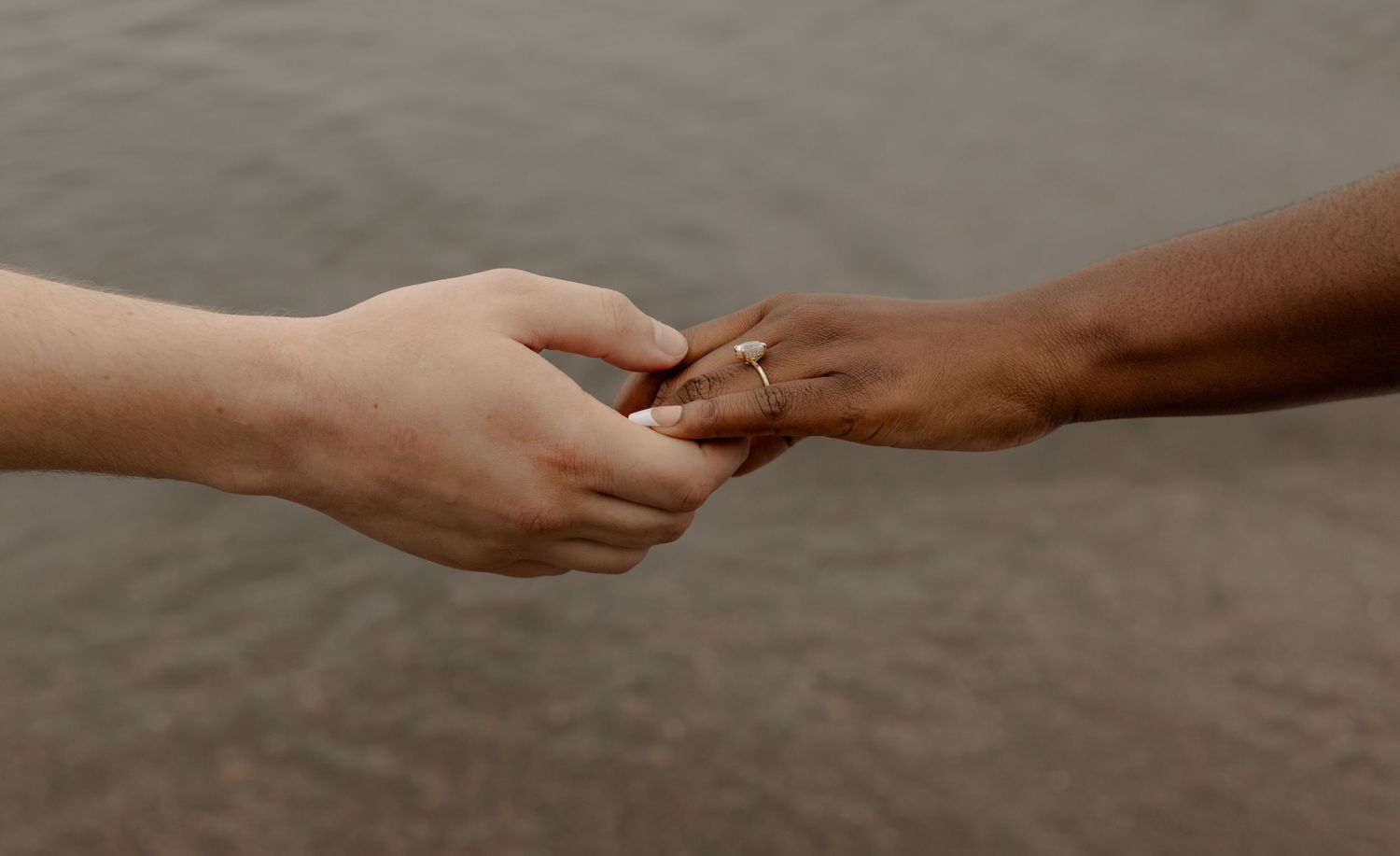 Close-up of hands exchanging or touching a ring against a water background.