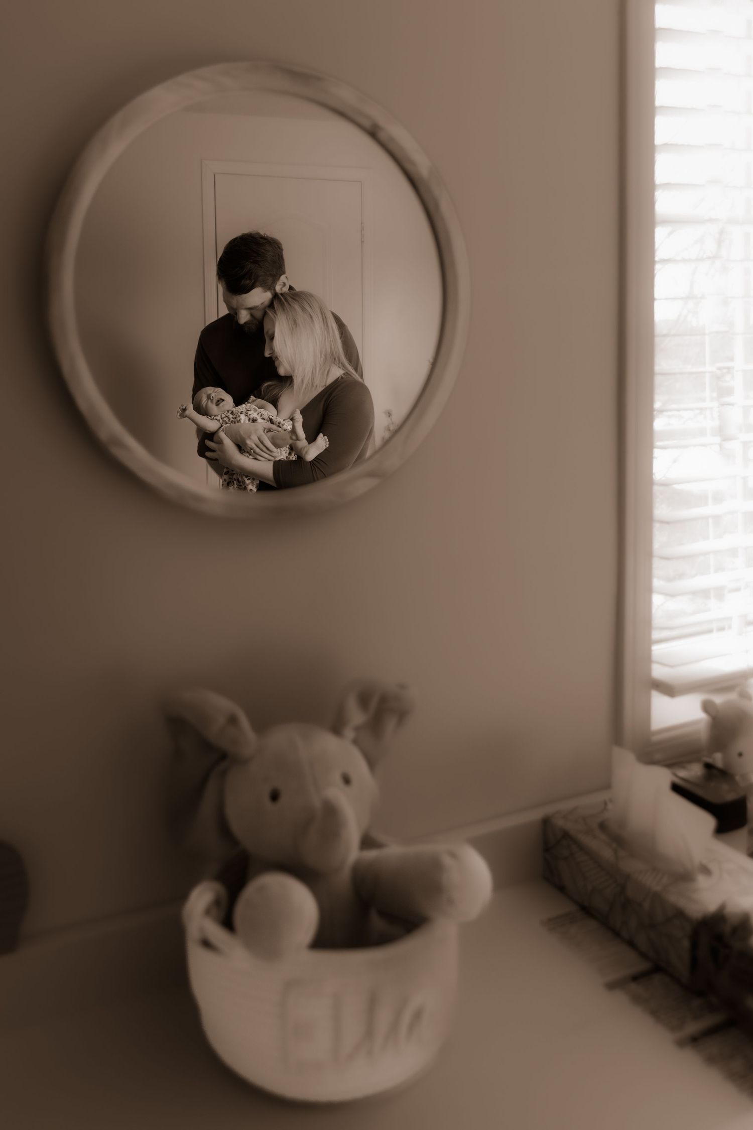 Circular mirror reflection shows a tender nursery moment with stuffed animals in foreground.