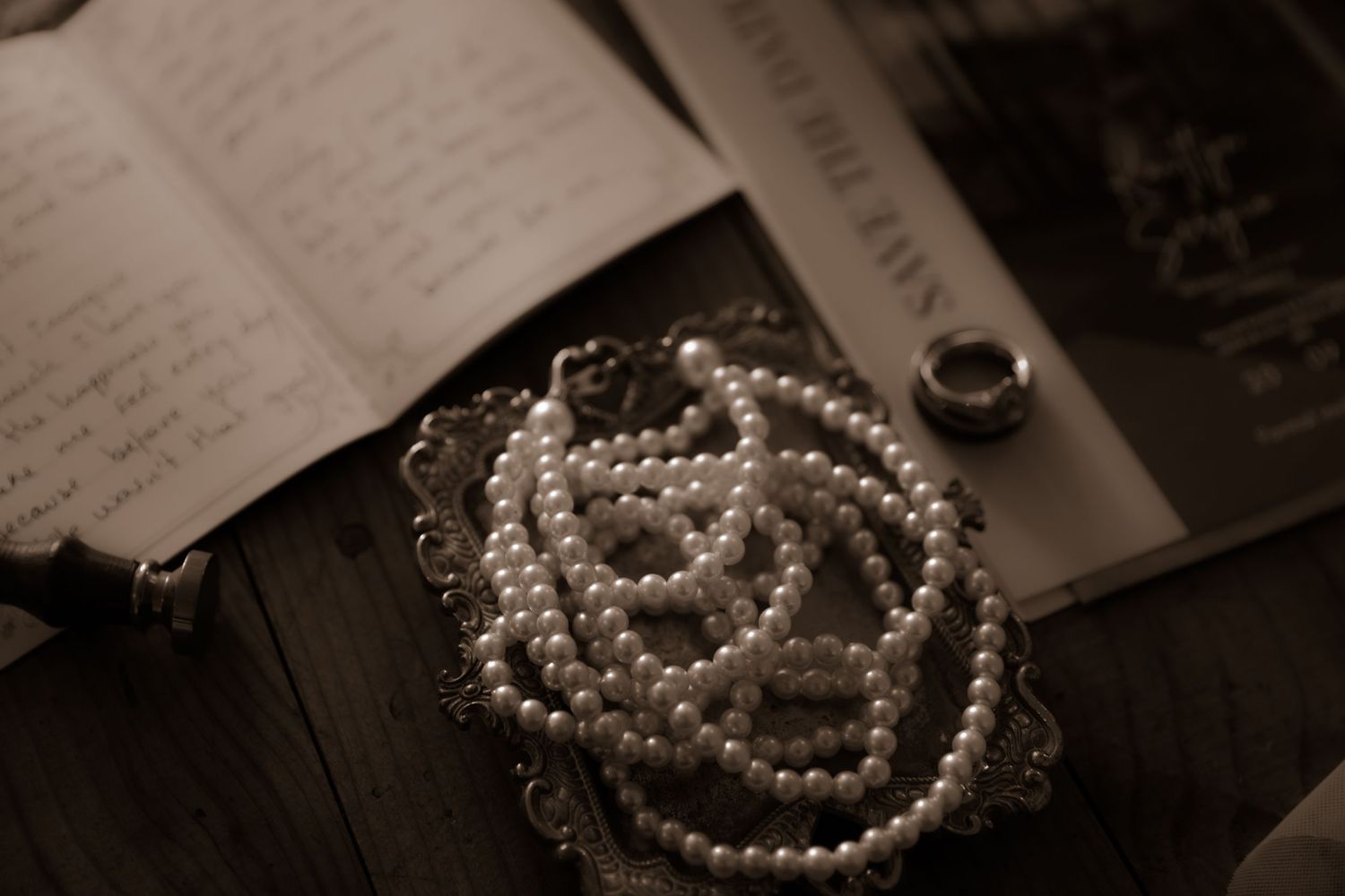 Pearl necklace arranged on antique frame with wedding details in sepia.