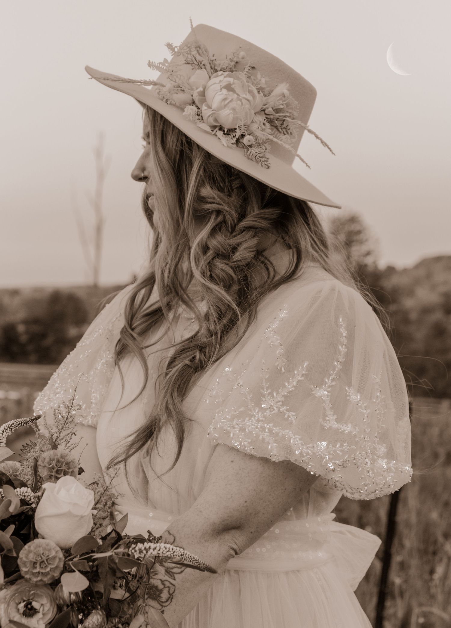 Vintage-style portrait of bride in white dress and floral hat holding bouquet.