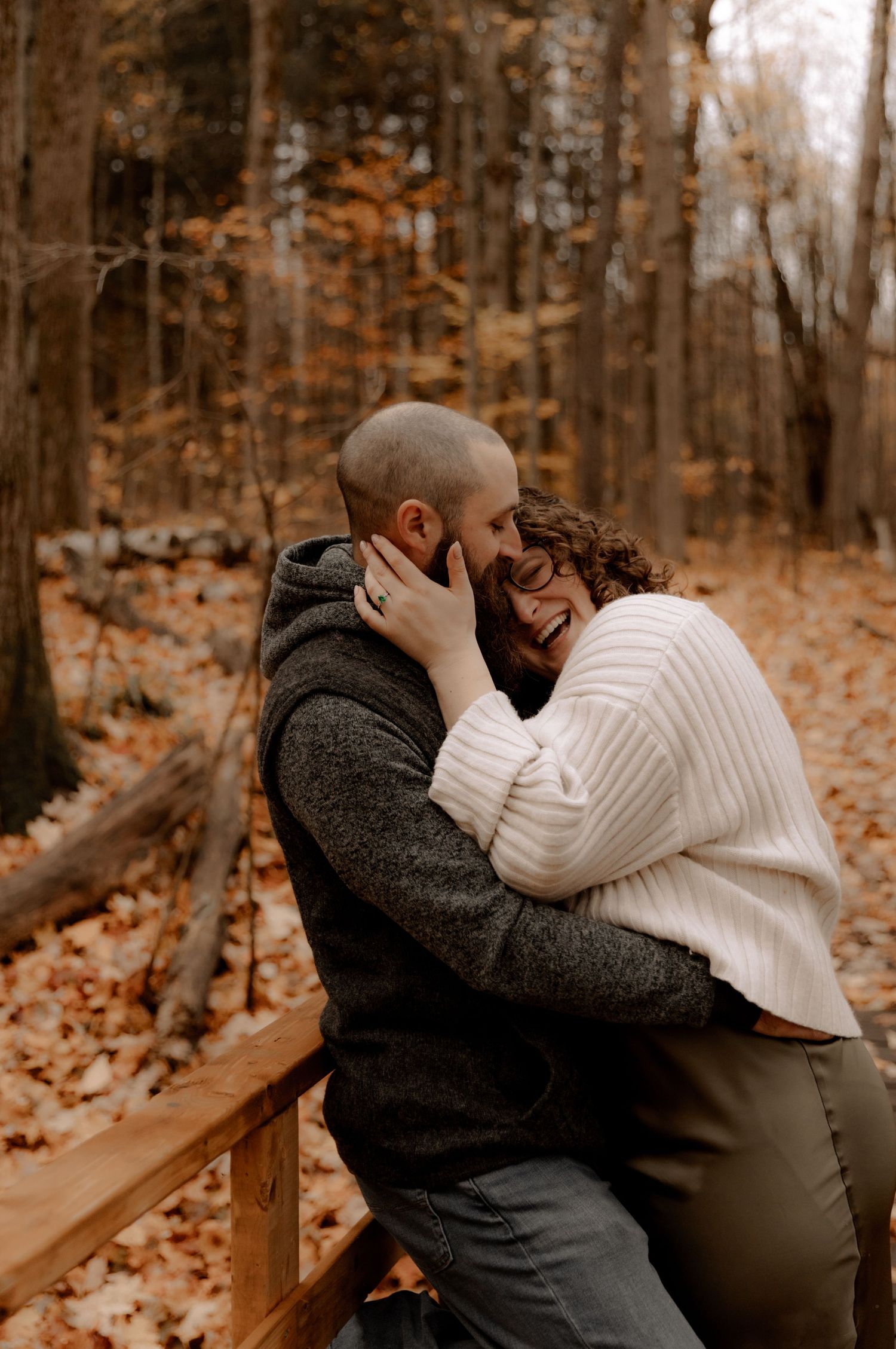 Intimate couple sharing tender moment on wooden bench in autumn forest surrounded by fallen leaves.