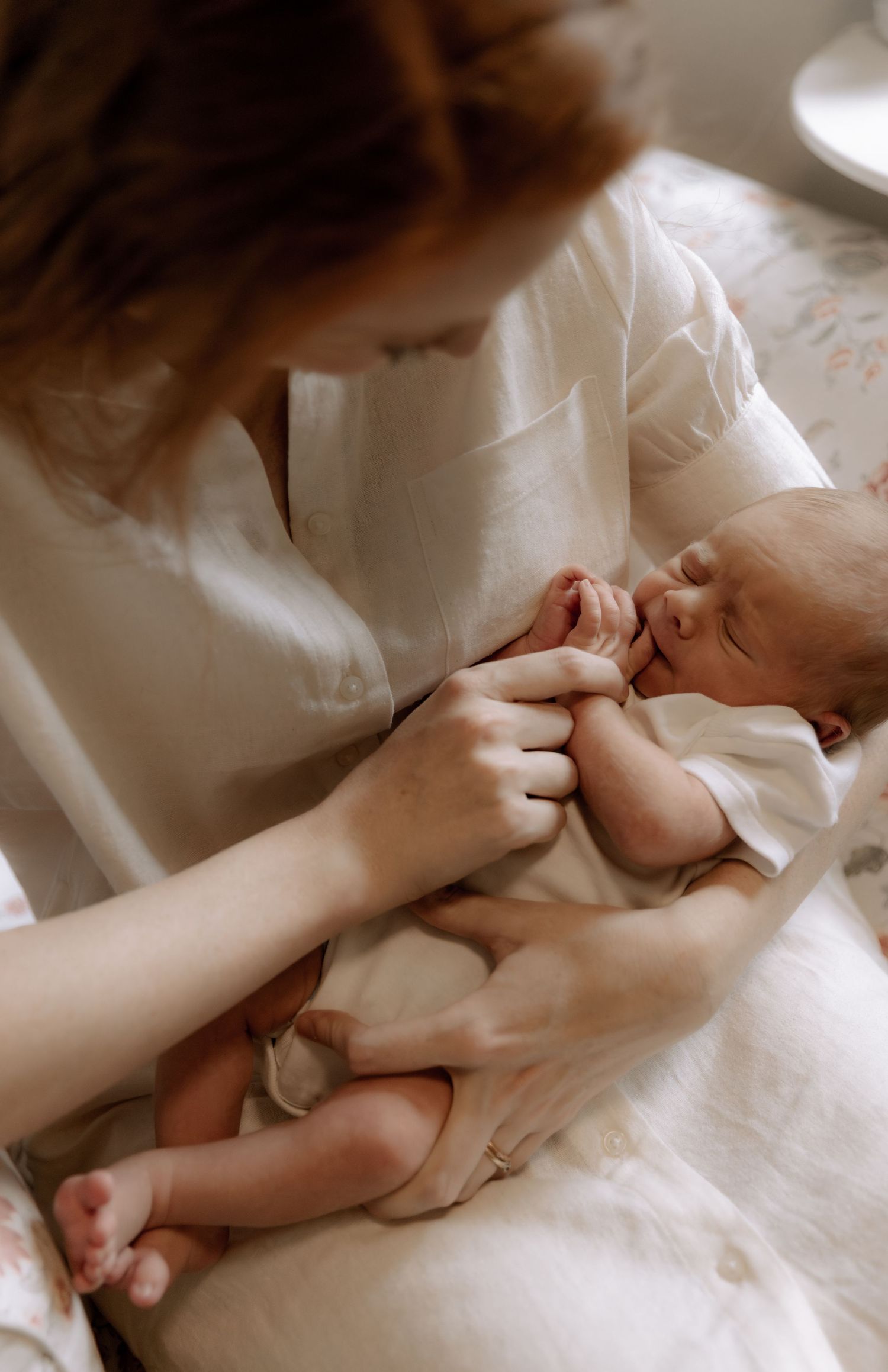 A tender moment showing gentle hands caring for a newborn baby wrapped in soft white fabric.