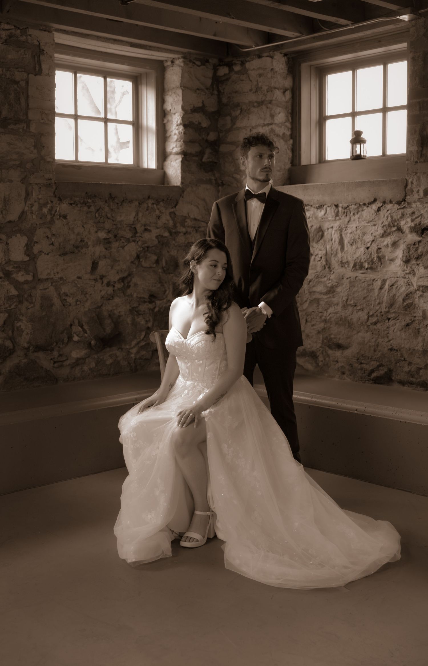 A classic black and white wedding portrait in a rustic stone room with natural window lighting.