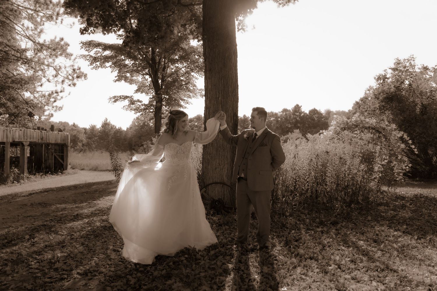 Sepia wedding photo of a couple standing together on a tree-lined path.