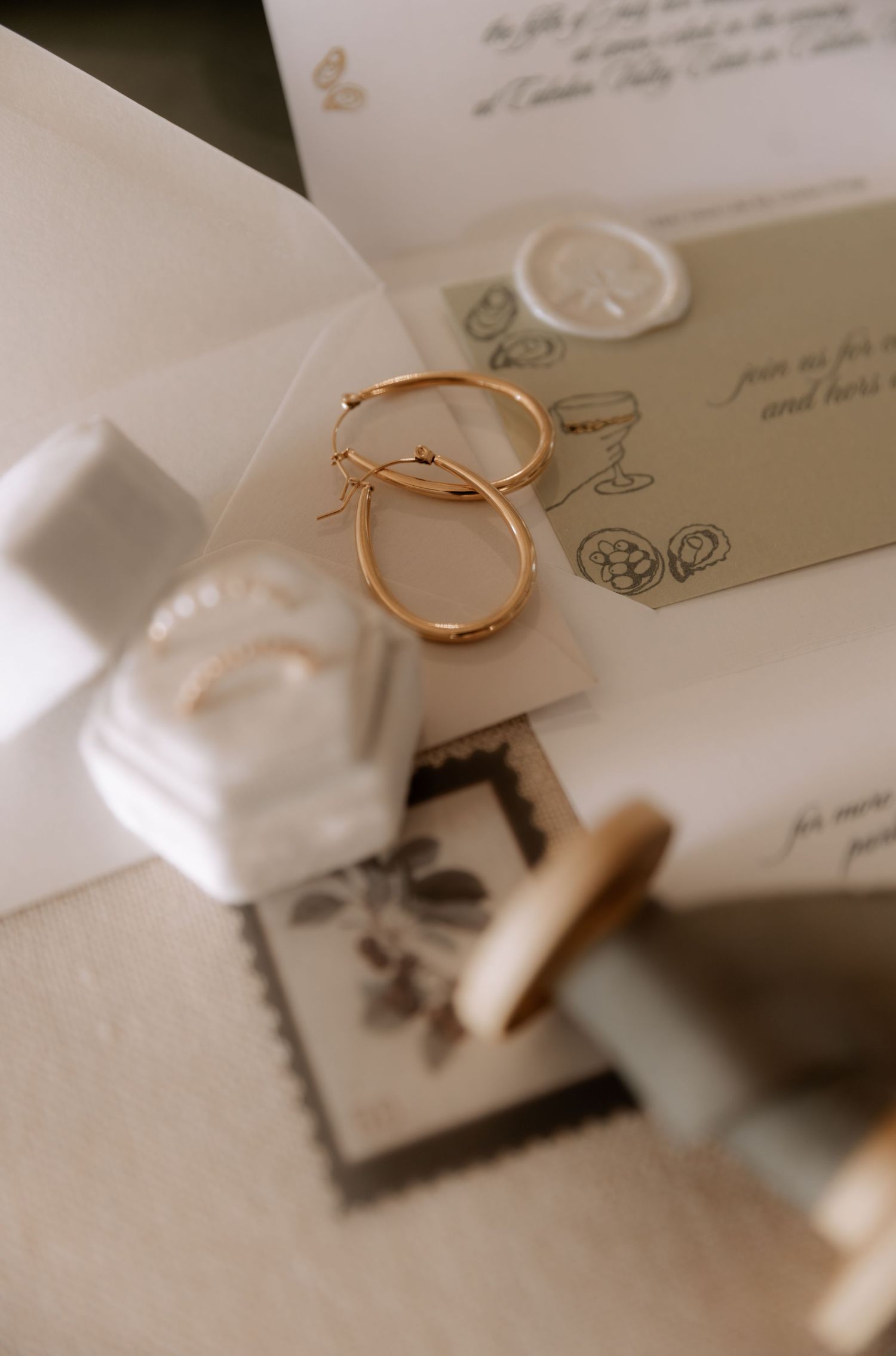 Gold wedding rings and invitation details artistically arranged on white fabric.