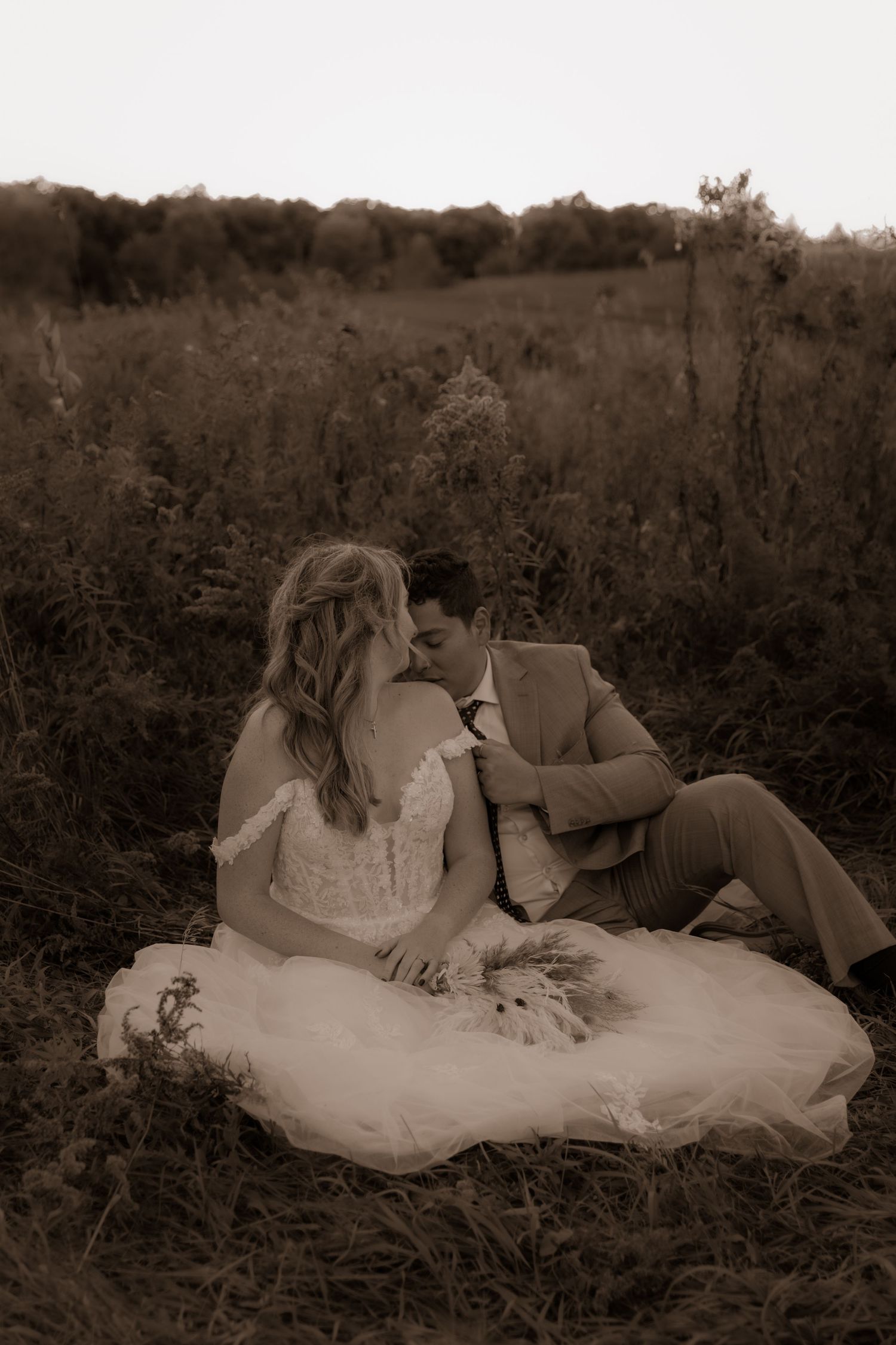 Couple shares romantic moment in sepia-toned field with flowing wedding dress.
