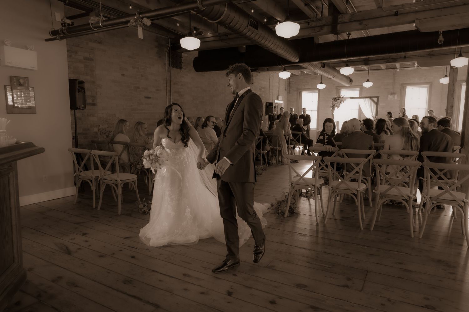 An intimate wedding moment captured in warm sepia tones inside a charming brick-walled venue.