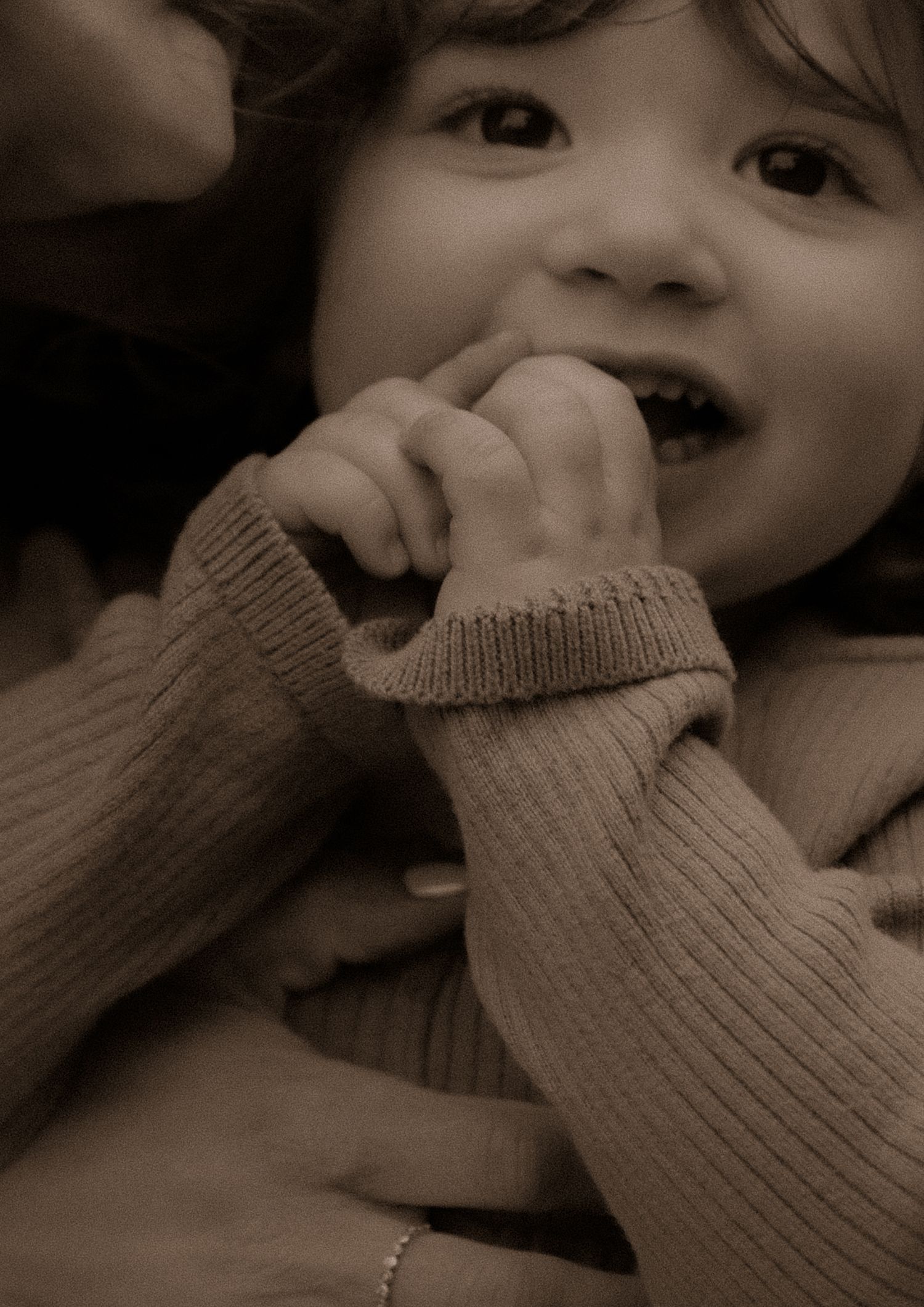 Sepia-toned portrait showing a bright smile and warm knit sweater detail.