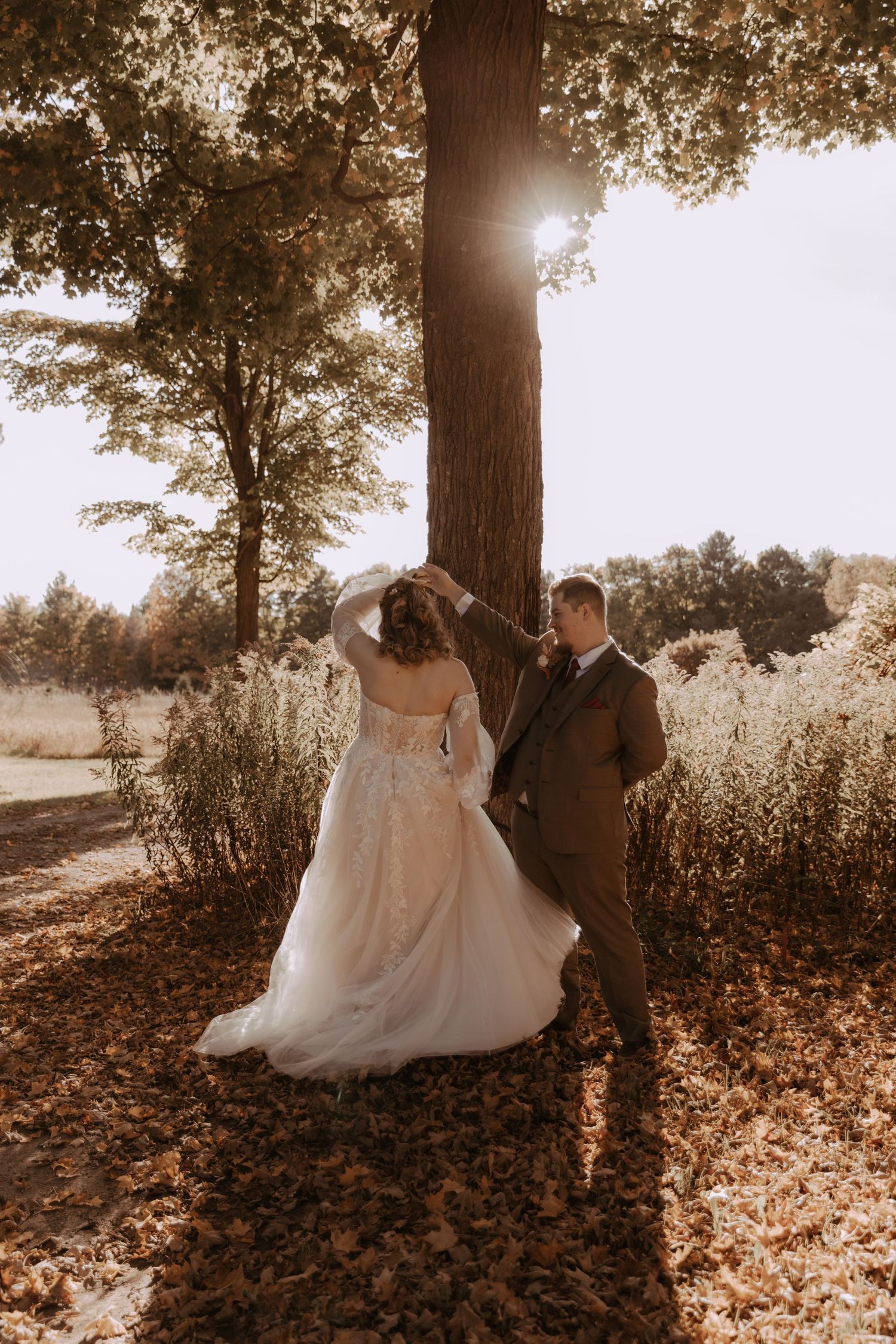 Newlyweds pose beside a large tree in warm autumn sunlight creating dramatic shadows in a rustic outdoor setting.