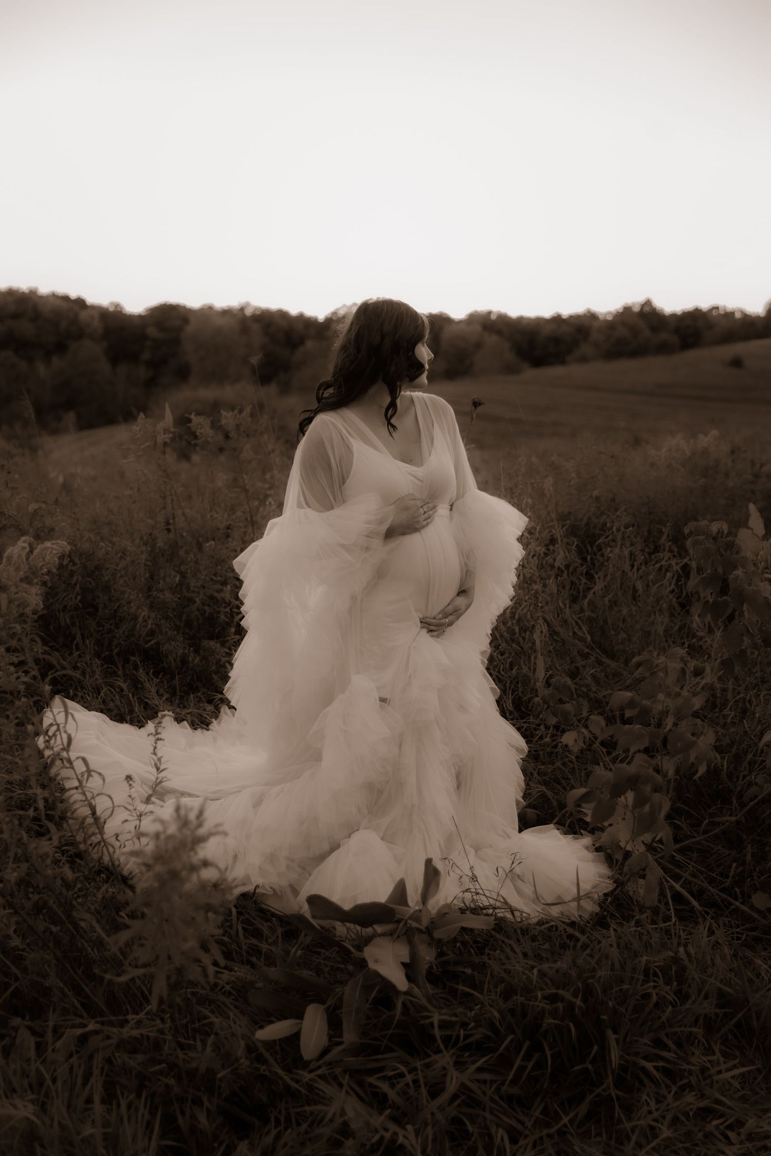 A dreamy sepia-toned photograph shows a flowing white gown billowing in the breeze against a rural hillside landscape.
