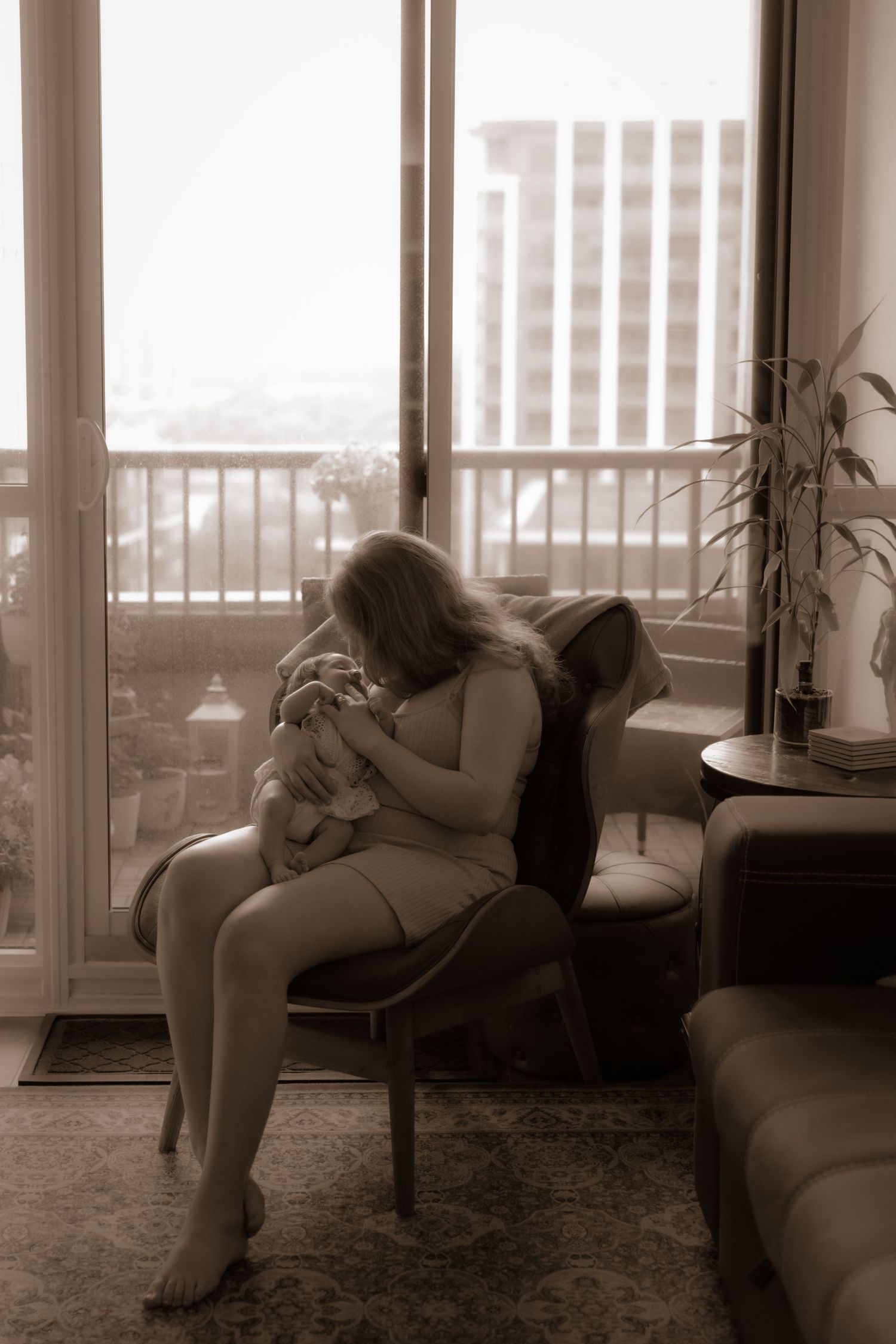 A monochrome photo showing a tender moment by a window in a living room with city buildings visible outside.