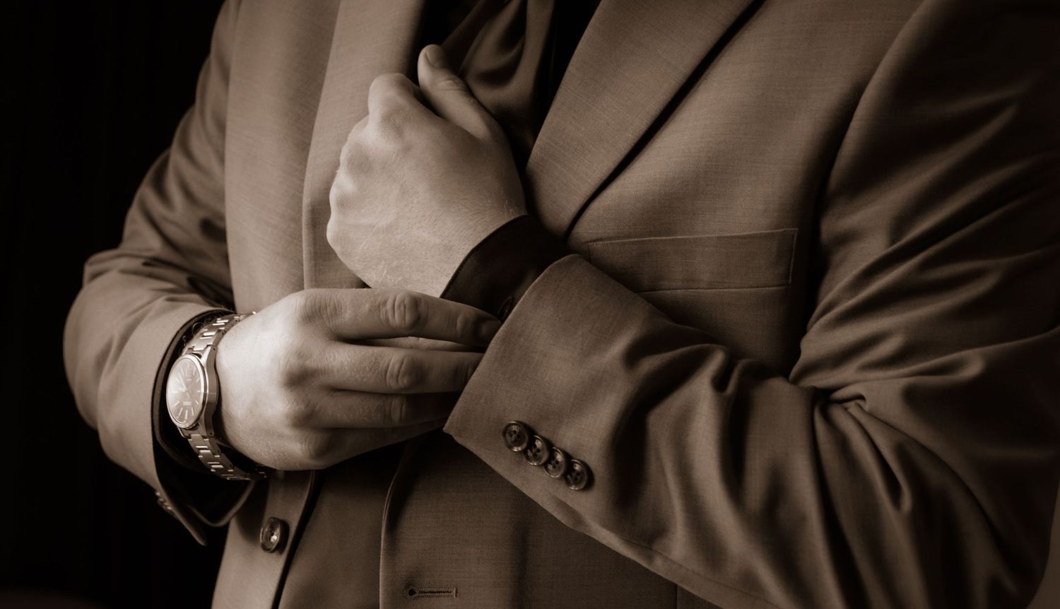 Close-up of hands adjusting formal suit jacket buttons in sepia tone.