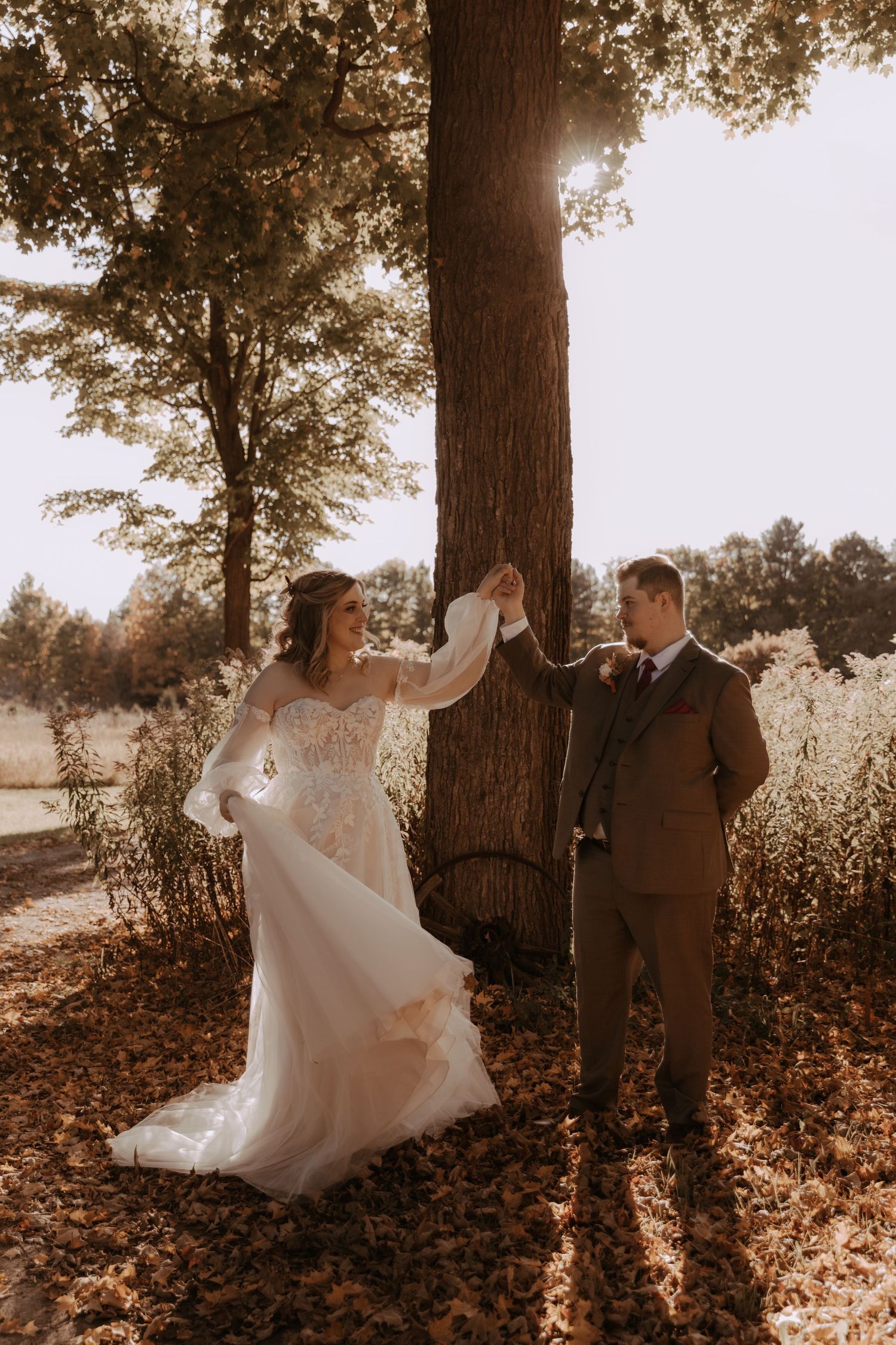 Wedding couple shares a joyful moment dancing around a tree in golden afternoon light.