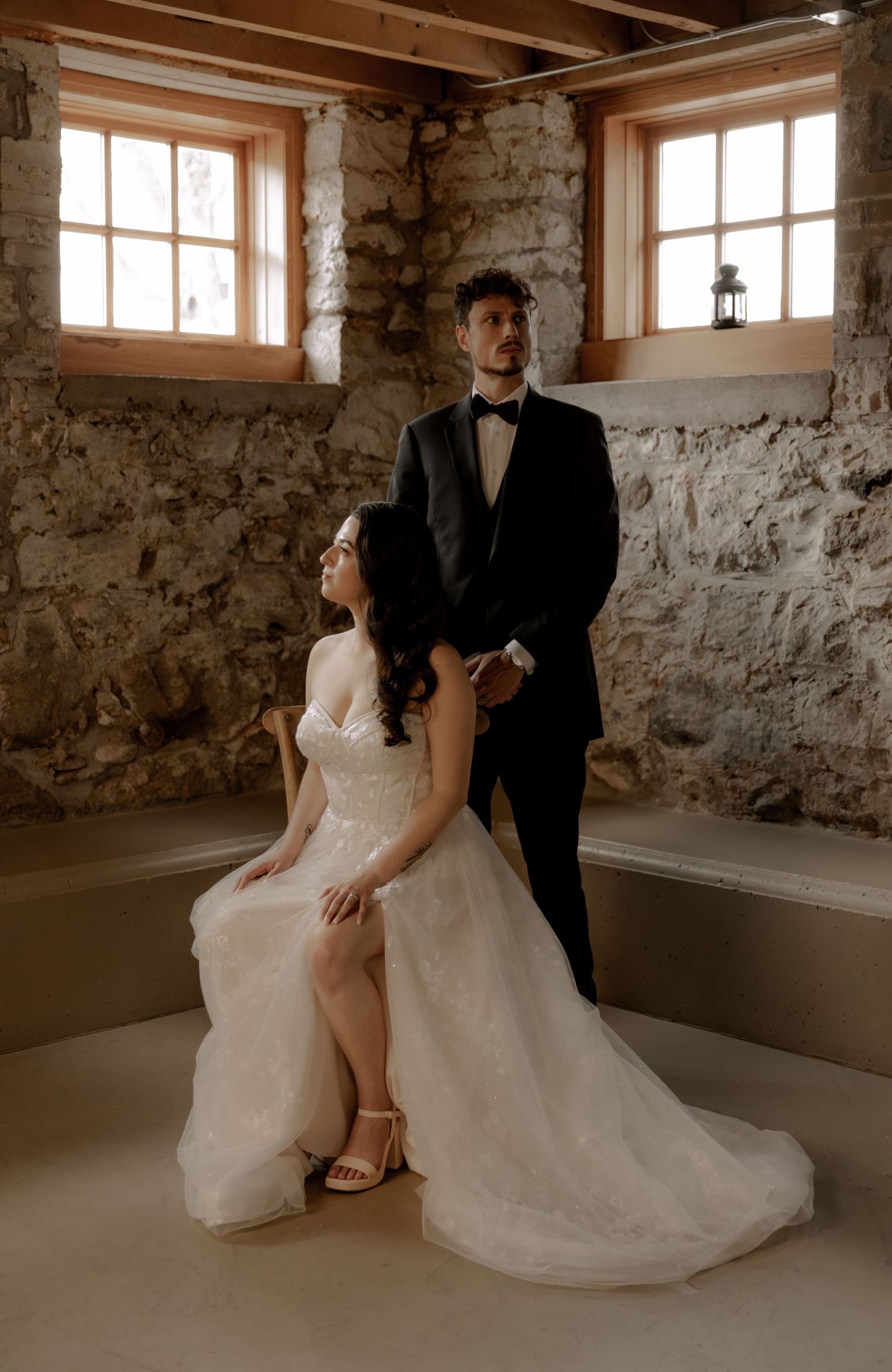An elegant wedding portrait in a rustic stone room with natural light streaming through small windows.