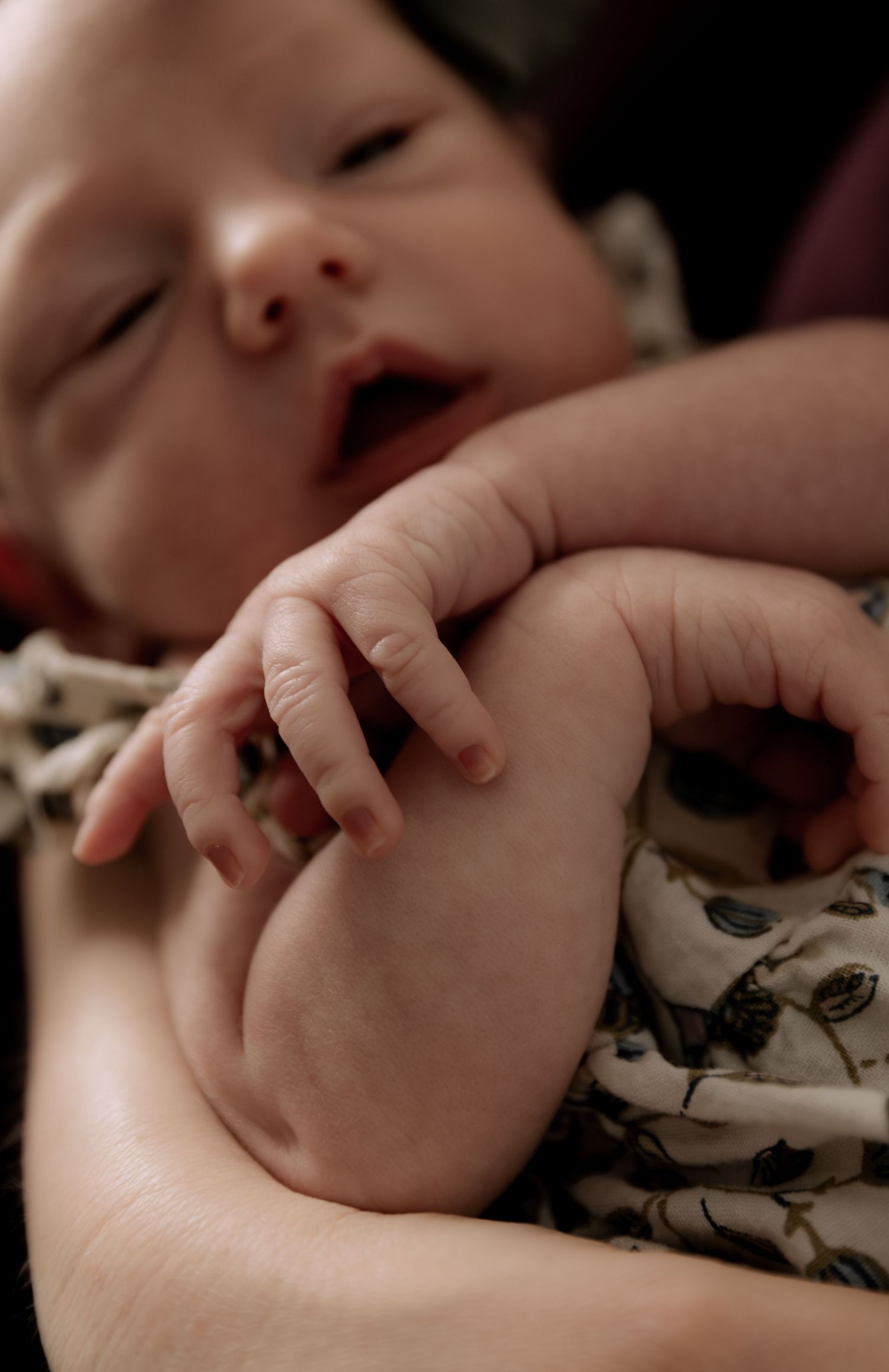 Close-up of a tiny hand grasping while resting on patterned fabric.