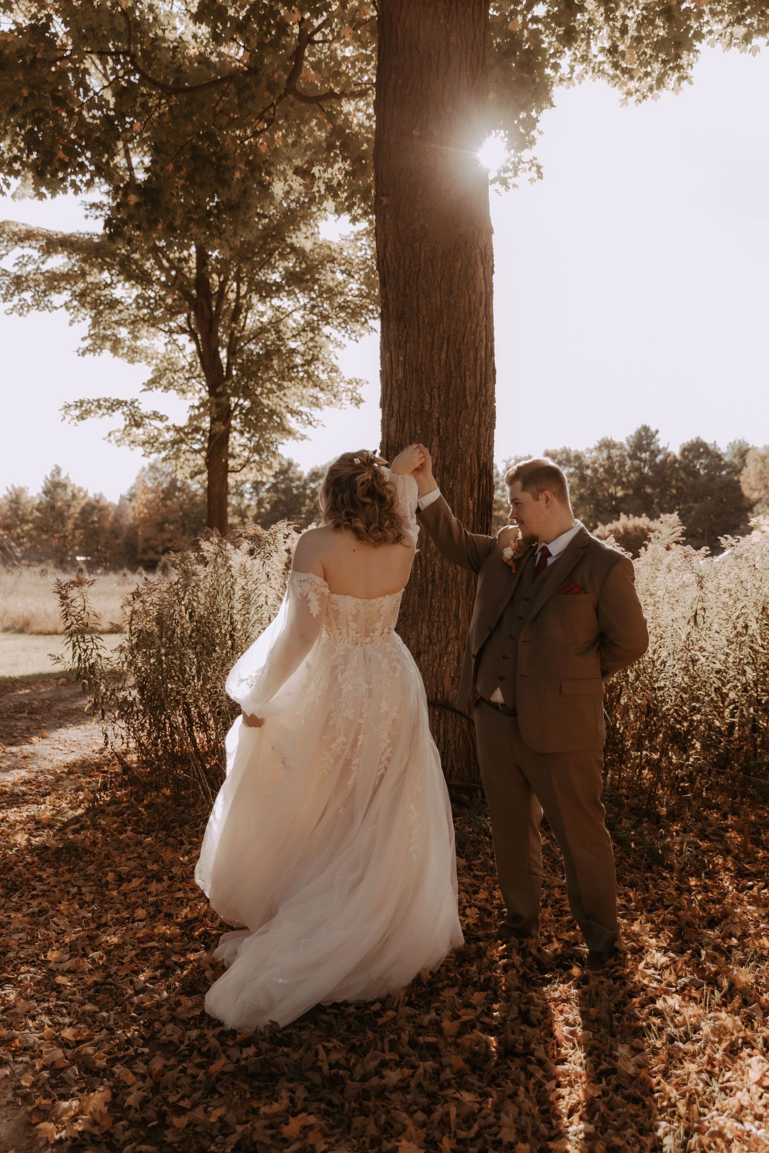 Sunlit autumn wedding portrait with couple standing beneath large tree.