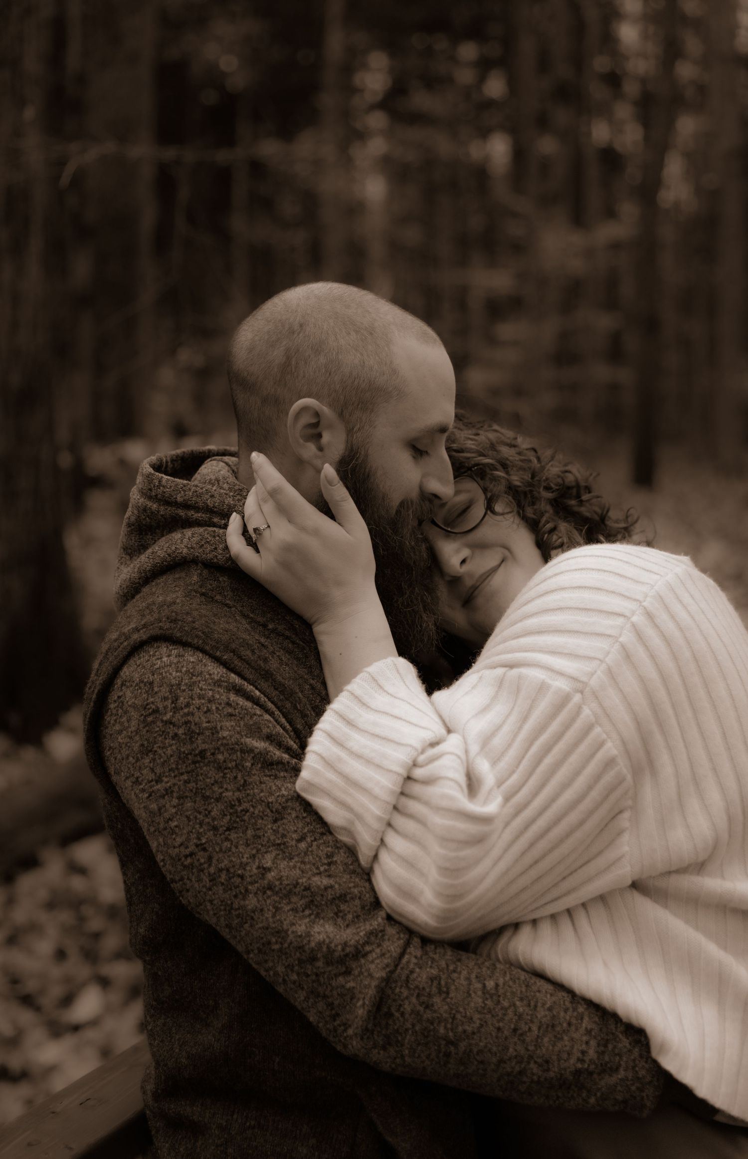 Sepia toned portrait of couple embracing on bench amidst autumn forest setting.