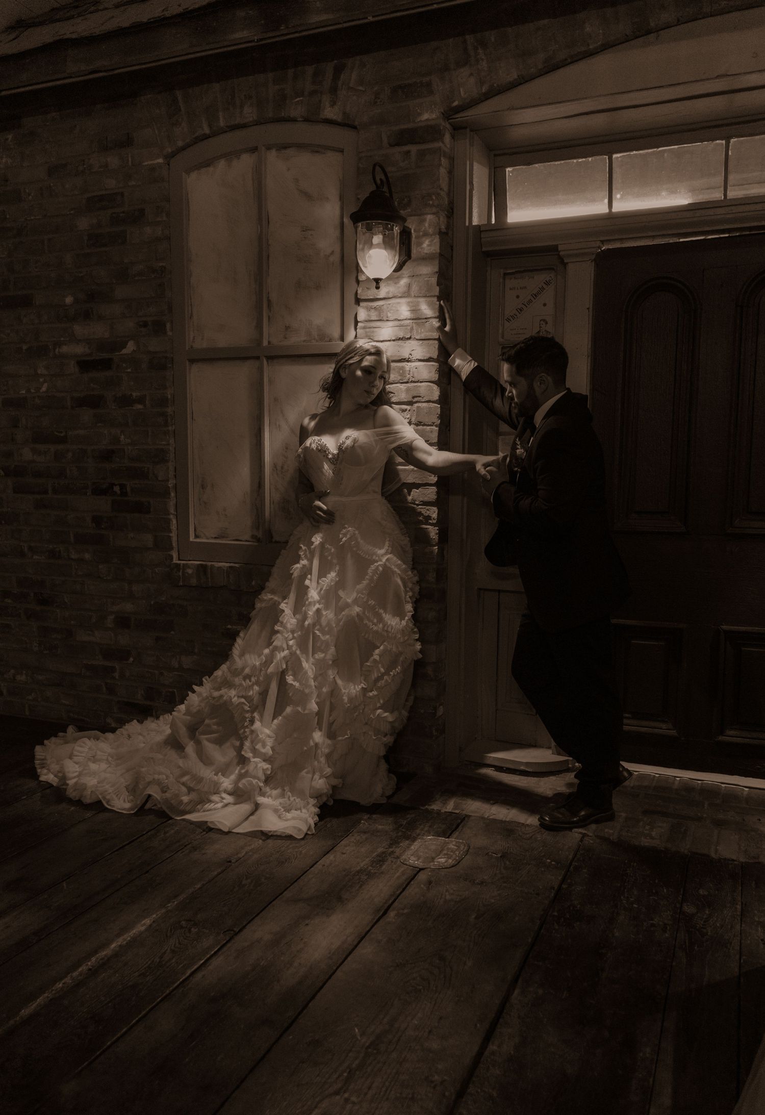 Romantic vintage scene with couple in formal wear posing near antique door and brick wall with lantern.
