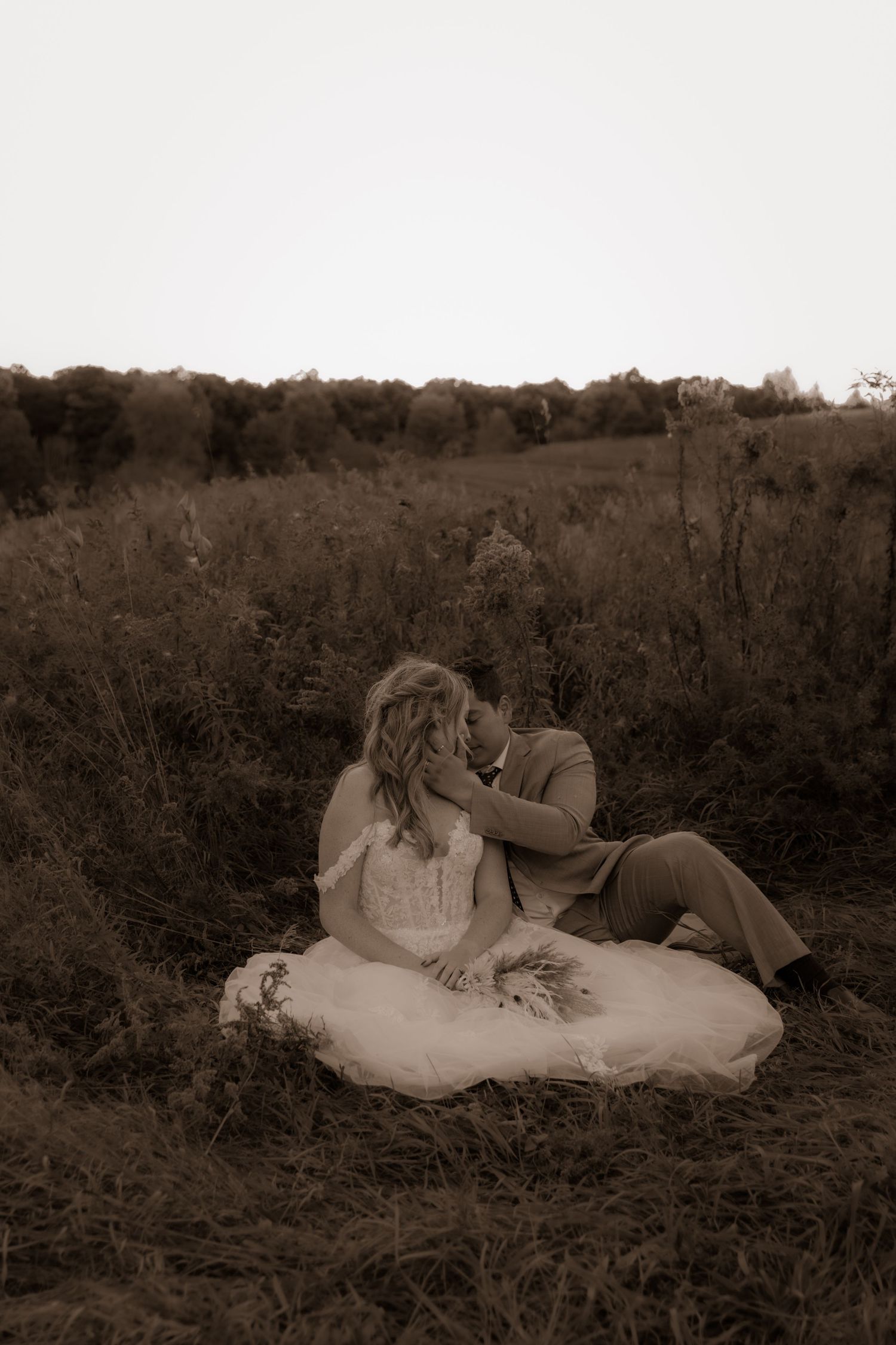 Romantic sepia portrait of couple sitting in wild grass field.