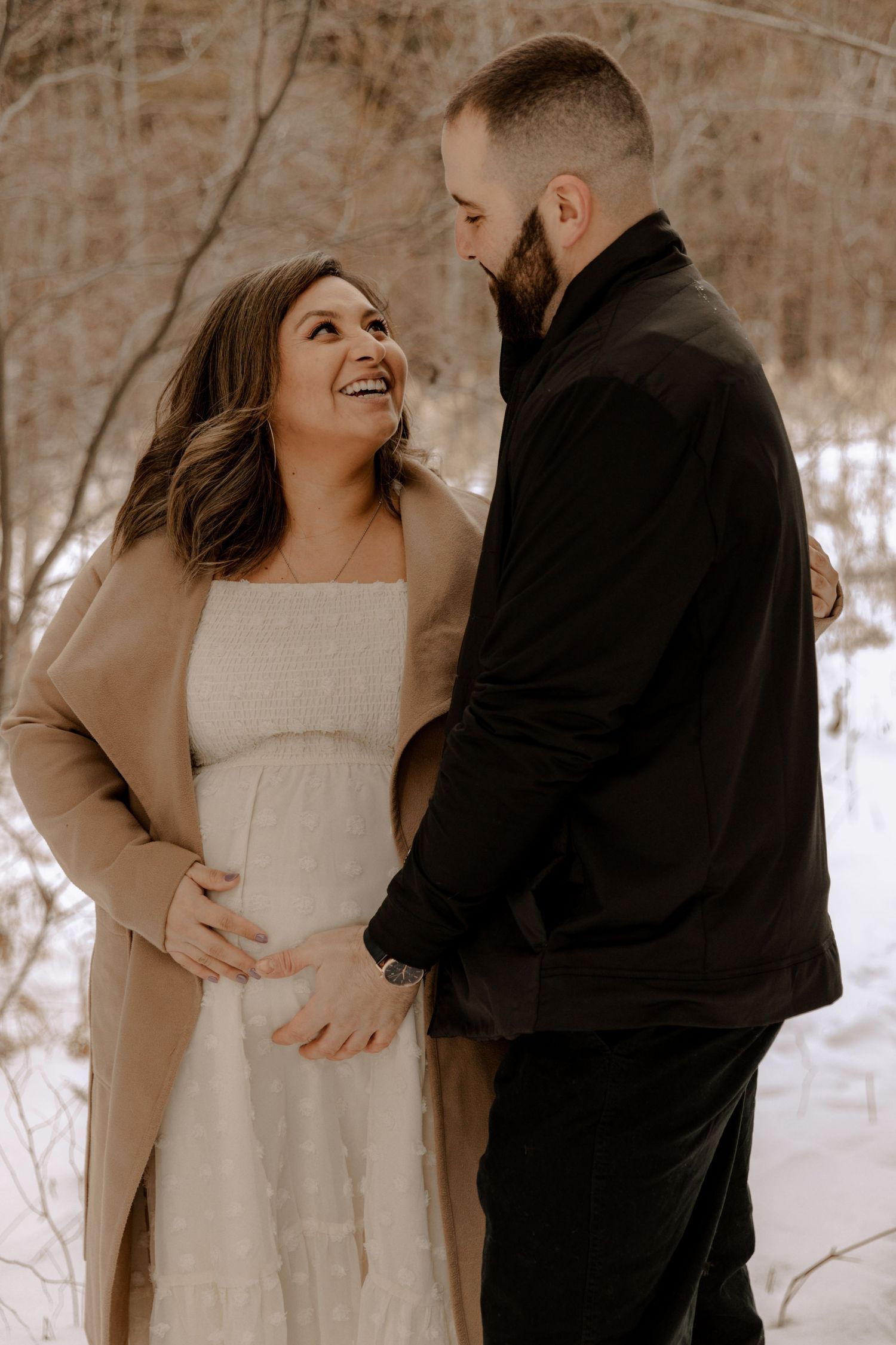A couple shares an intimate moment in nature during their maternity photo session wearing cozy winter attire.