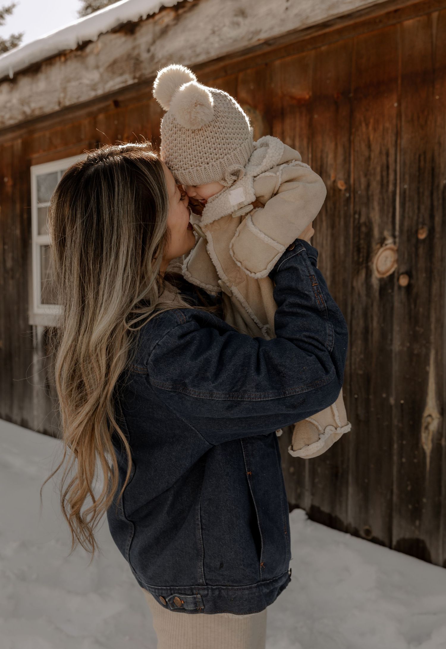 A tender winter moment outside a snowy cabin showing affection between parent and child in coordinated winter outfits.