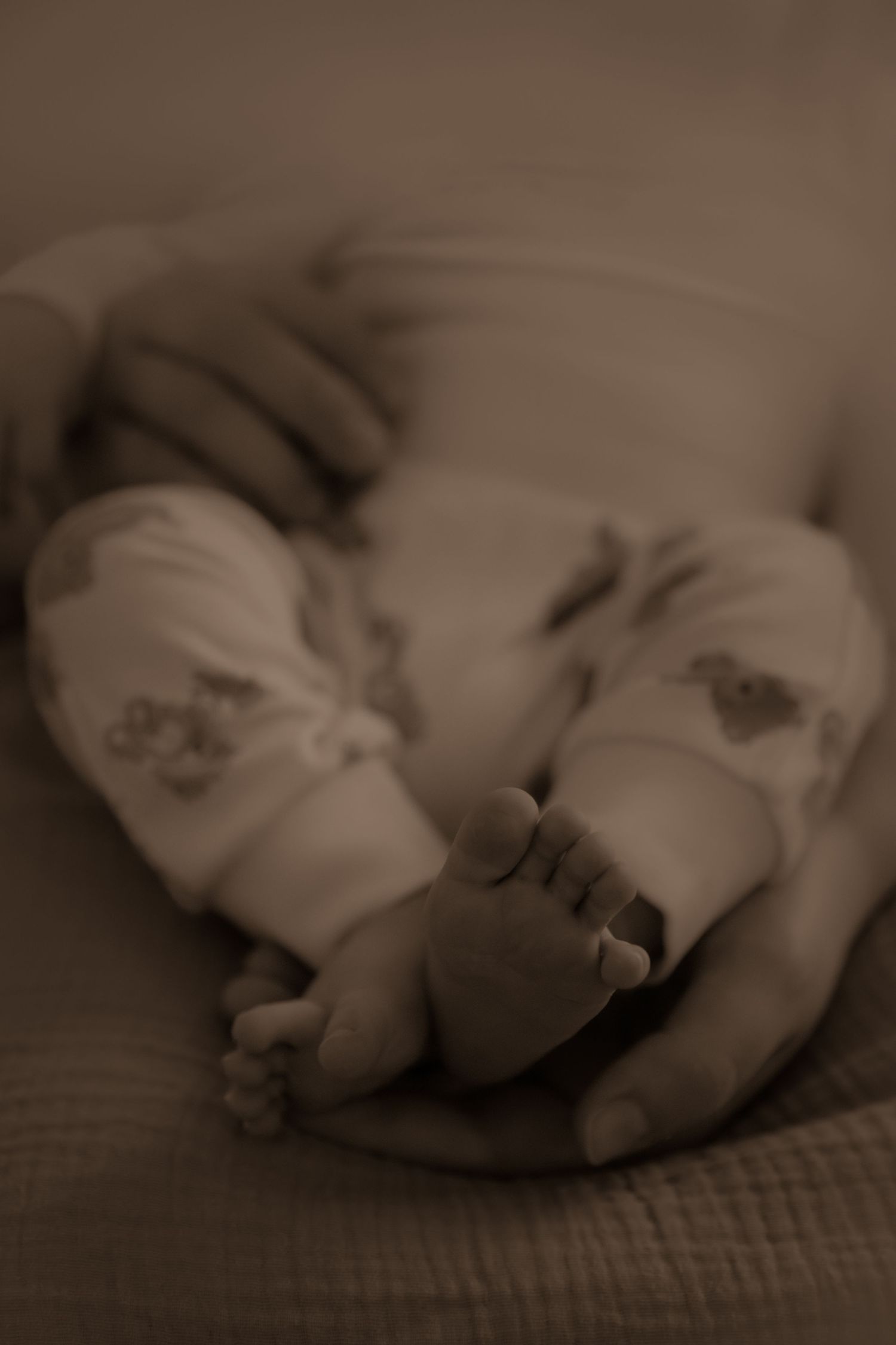 Close-up sepia photograph of tiny baby feet in white socks resting gently on soft textured fabric.
