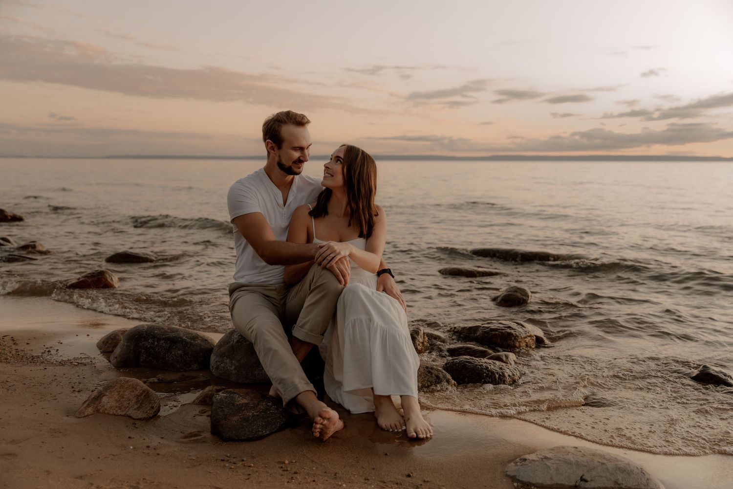 Romantic couple sitting on coastal rocks during golden hour by the ocean.