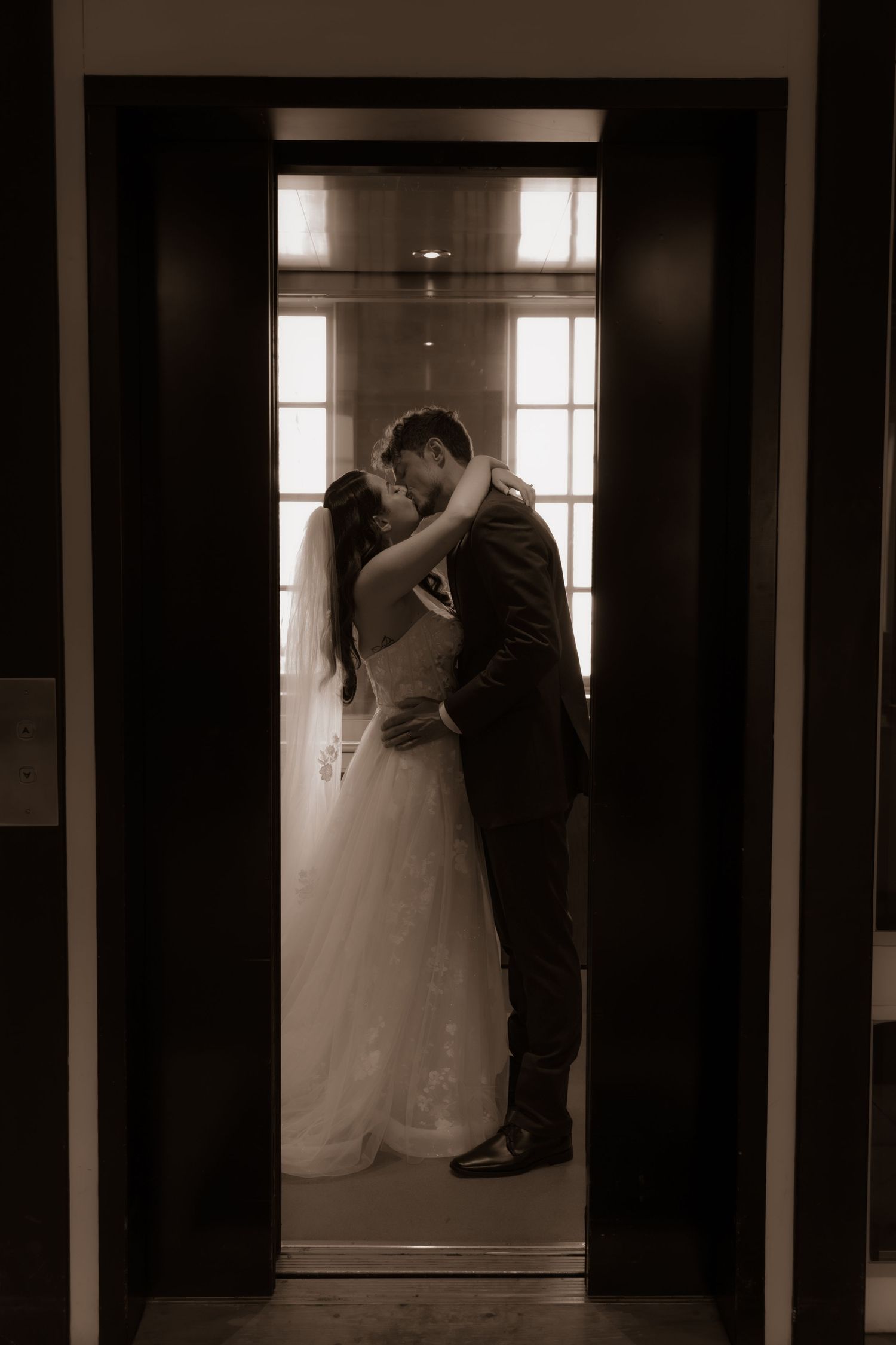 A romantic couple sharing an intimate moment in a doorway with natural backlight on their wedding day.