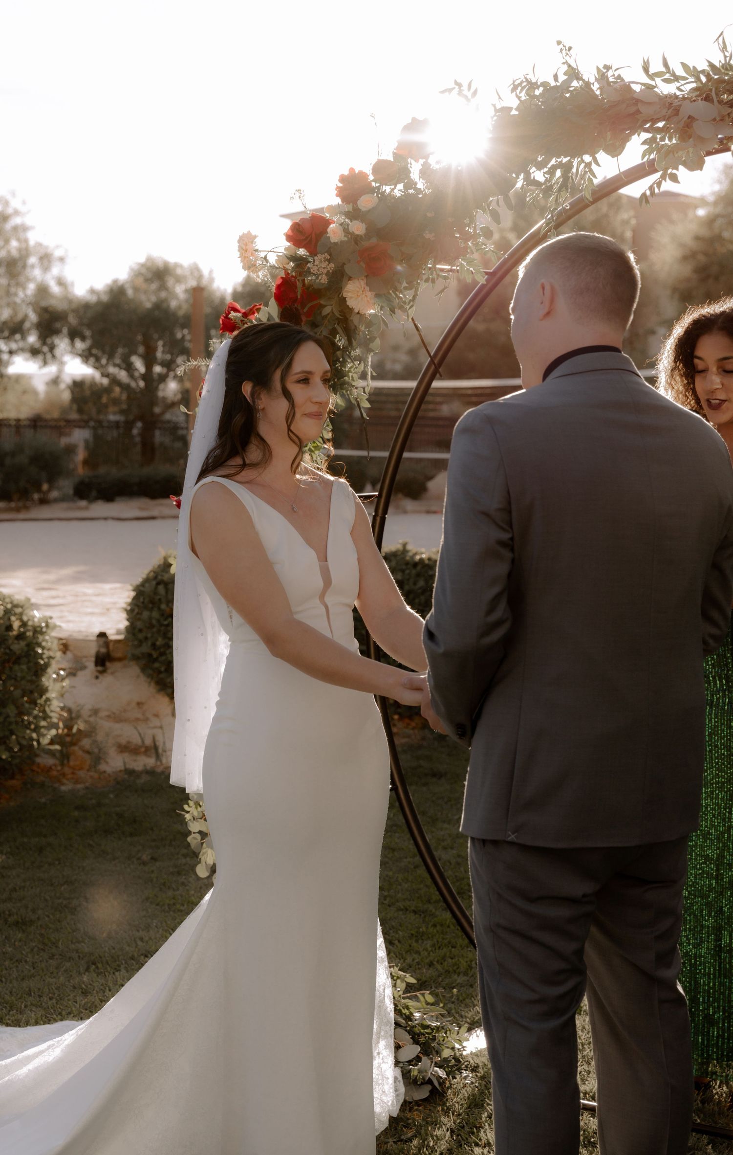 A sunset wedding ceremony with bride and groom standing under a floral arch.