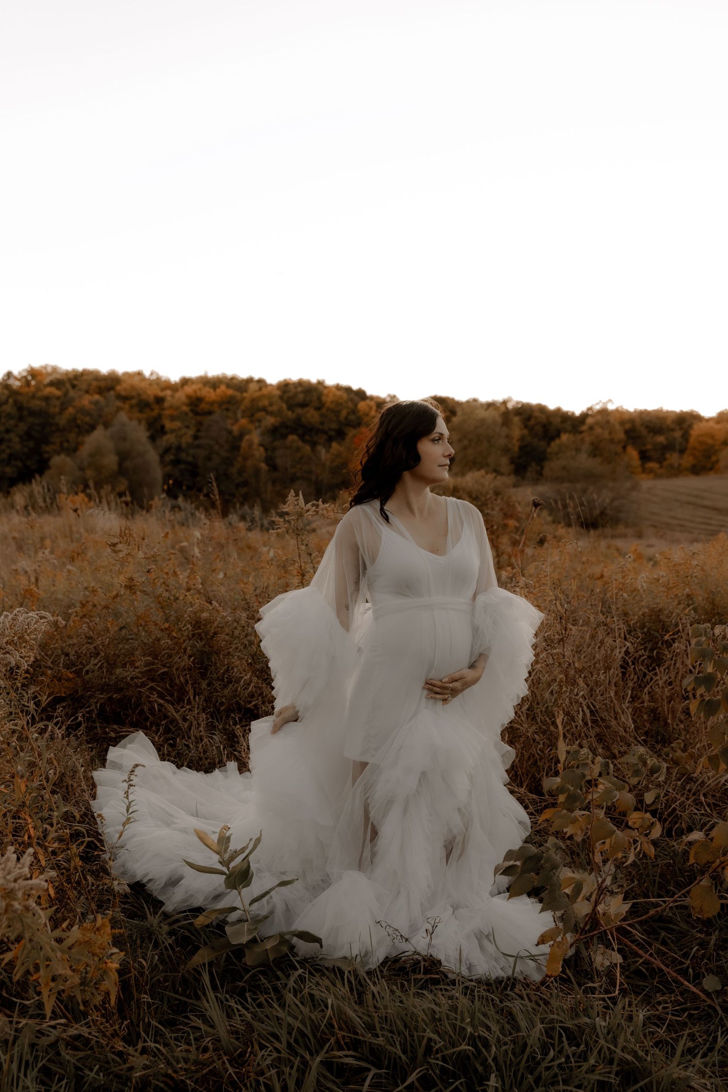 Ethereal wedding dress photograph with flowing tulle details in golden field at sunset.
