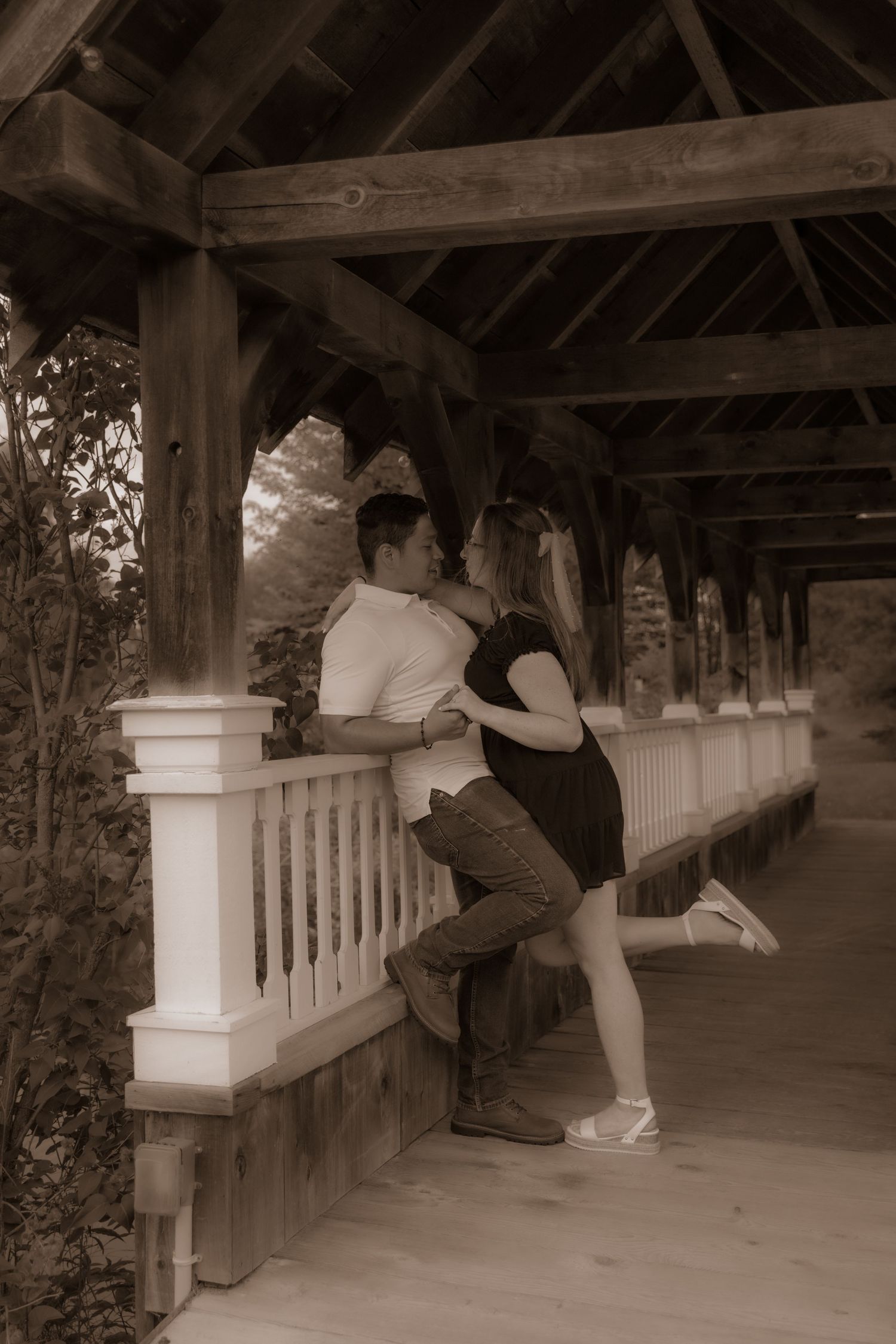 A couple shares a romantic moment on a covered wooden porch with white railings in sepia toned photography.