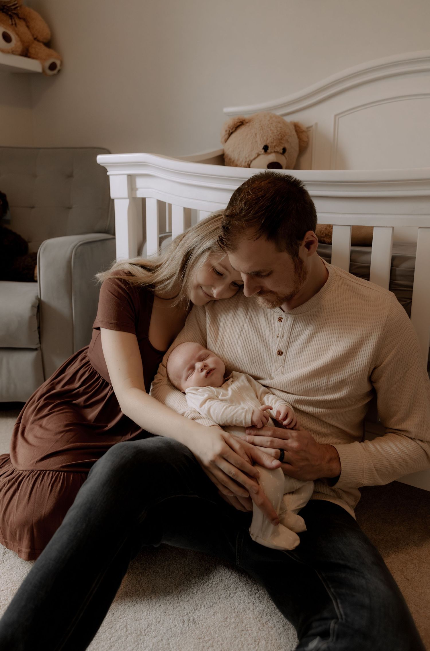 Parents share an intimate moment with their newborn baby in a cozy nursery setting next to a white crib.