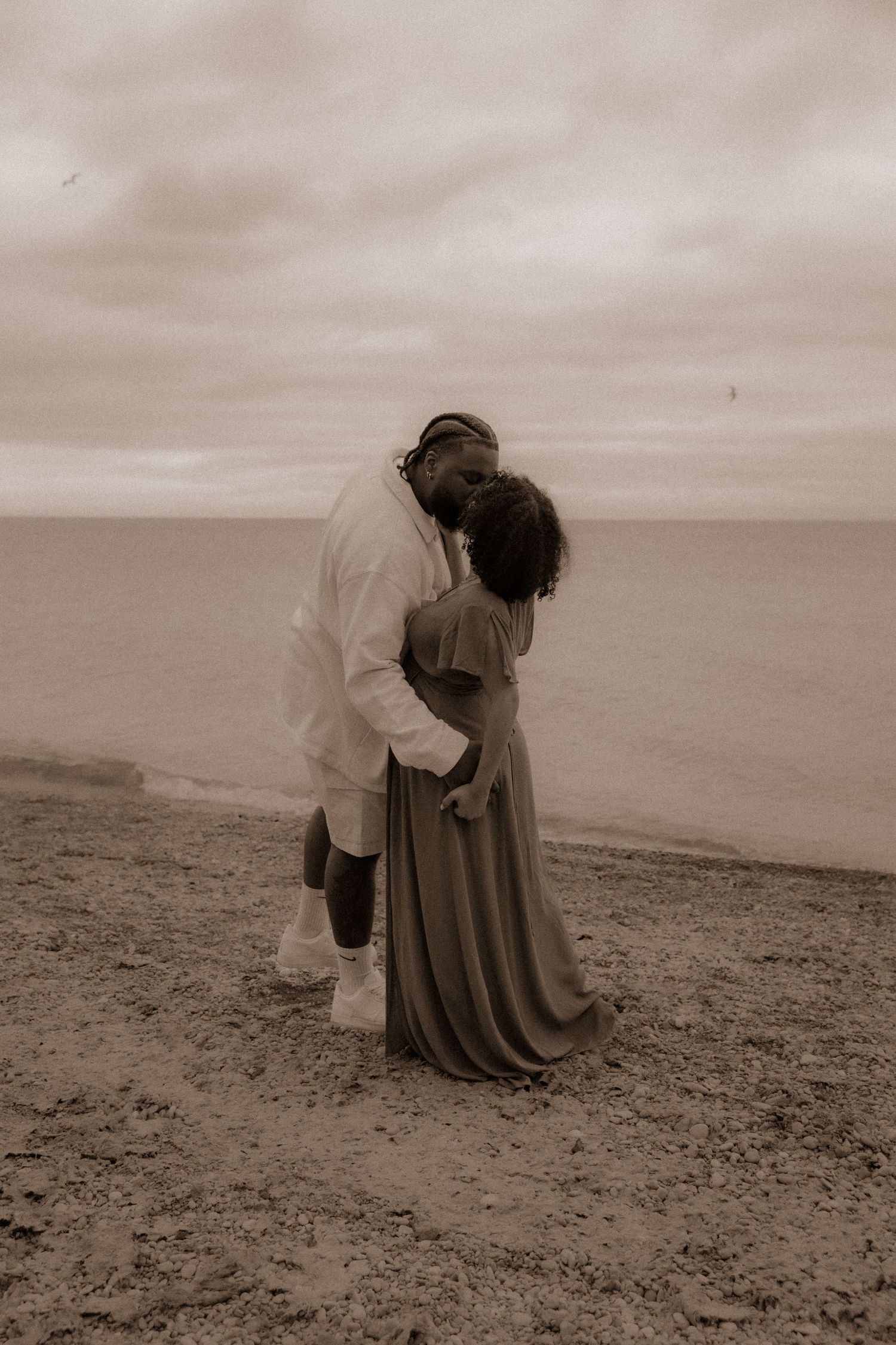 A tender moment captured in sepia tones on a cloudy beach day.