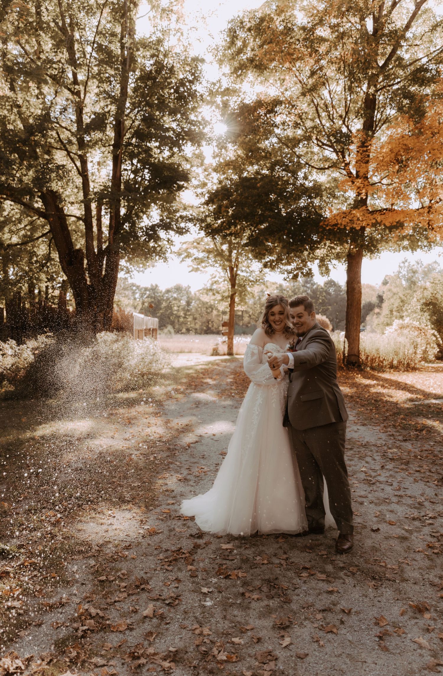 A romantic autumn wedding photo on a tree-lined dirt path.