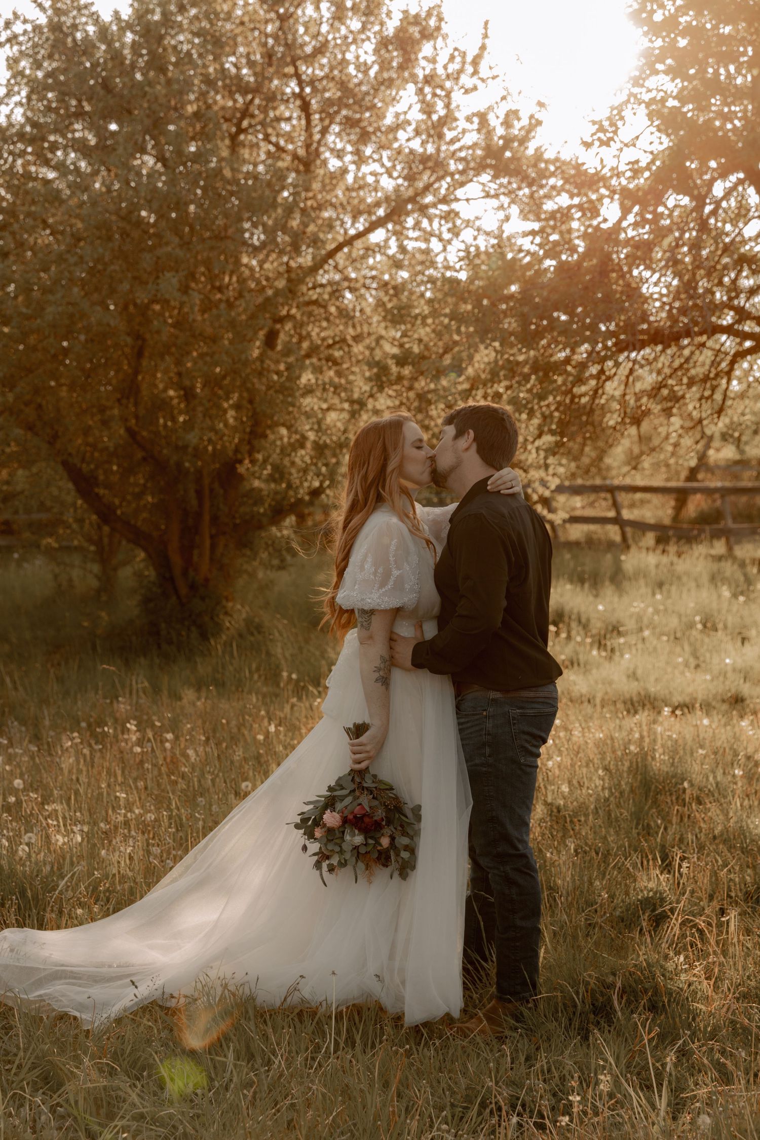 Dreamy wedding portrait with couple standing among orchard trees at sunset.