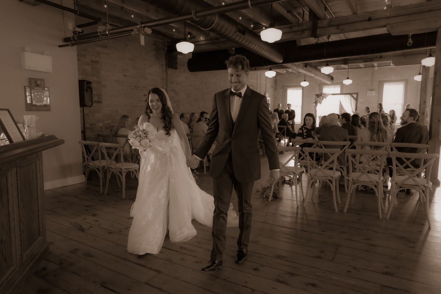 A couple walking together in a rustic indoor venue with wooden floors and industrial lighting.