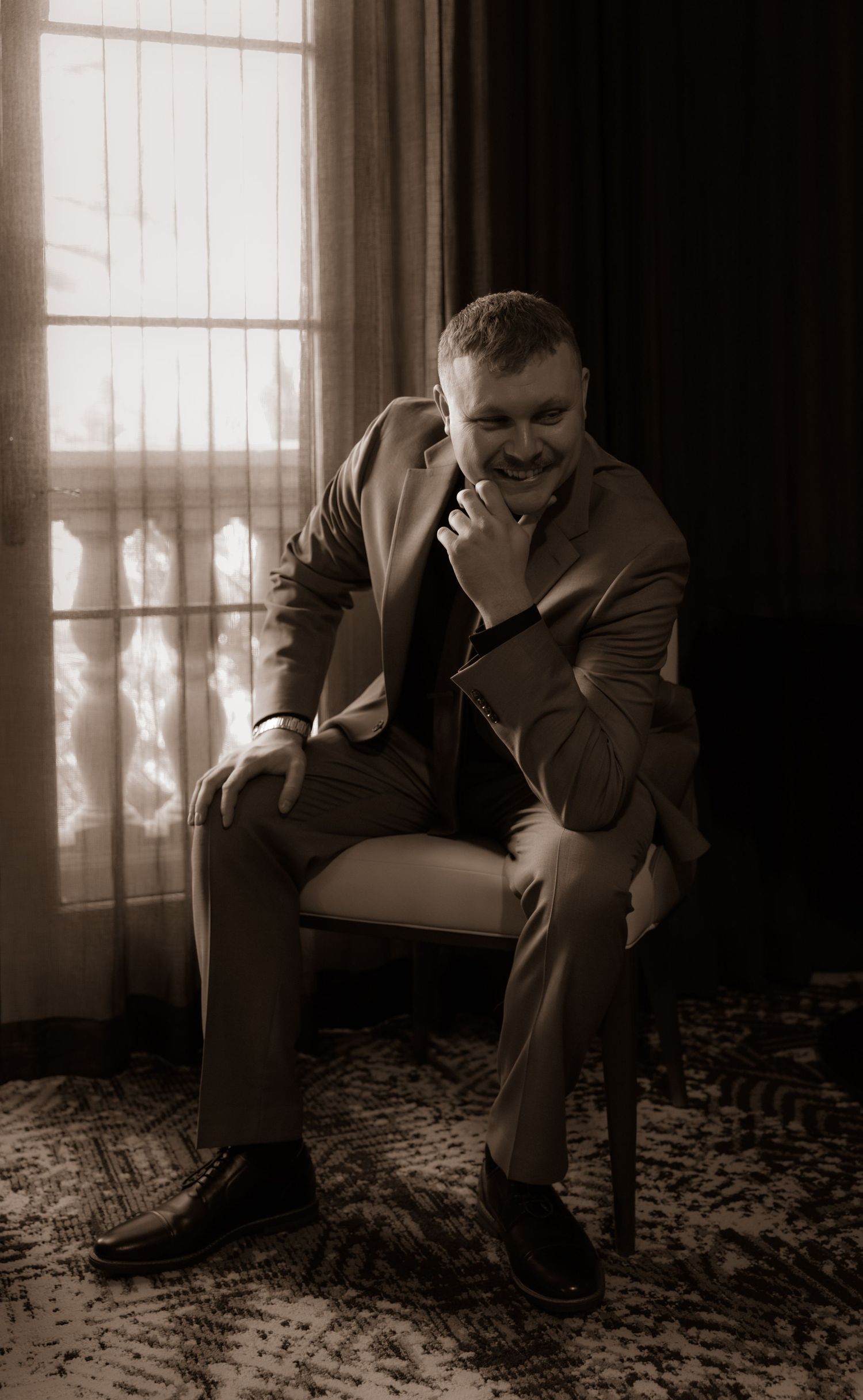 A contemplative moment captured in sepia of someone seated by a window in business attire.