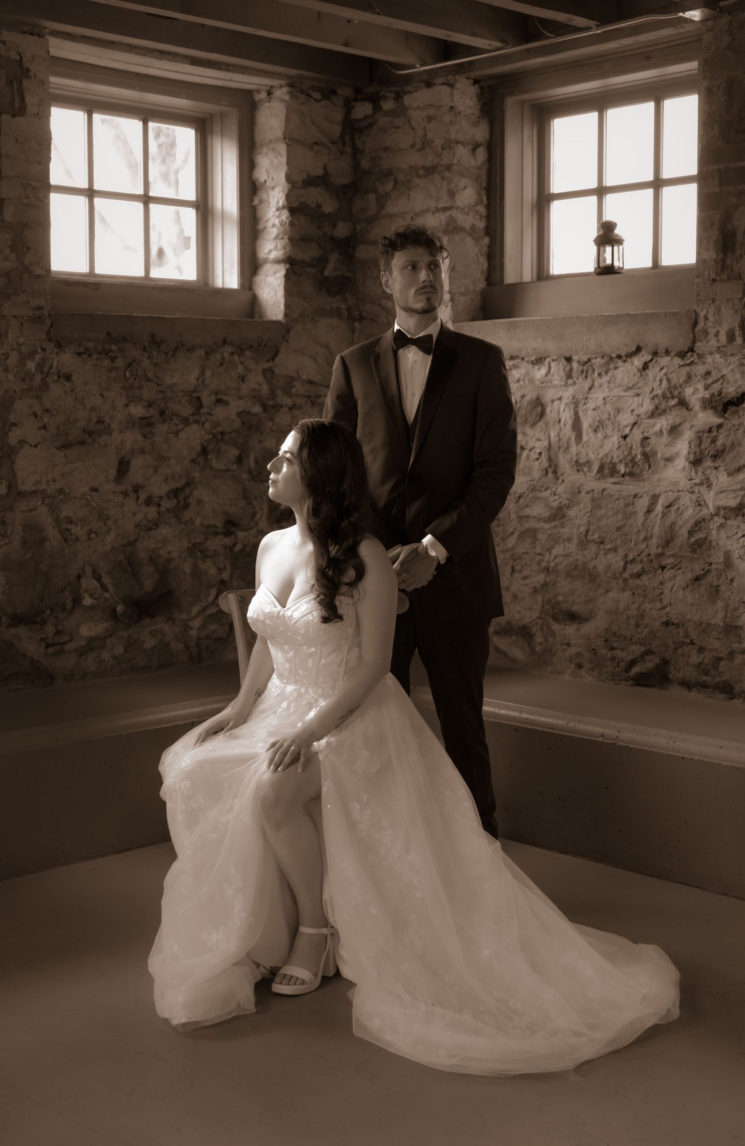 Classic wedding portrait in a vintage stone room with dramatic window lighting.