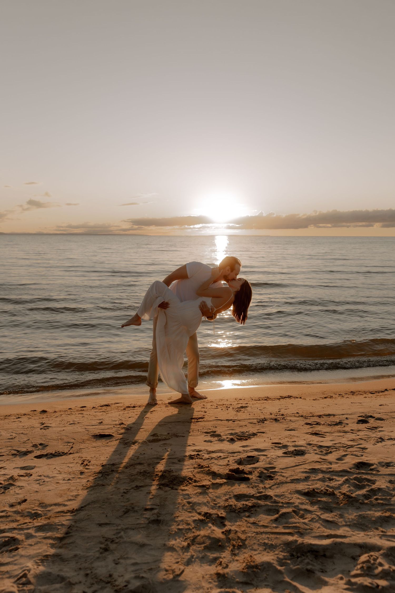 A romantic sunset beach scene with a couple in white creating a silhouette against the golden horizon.