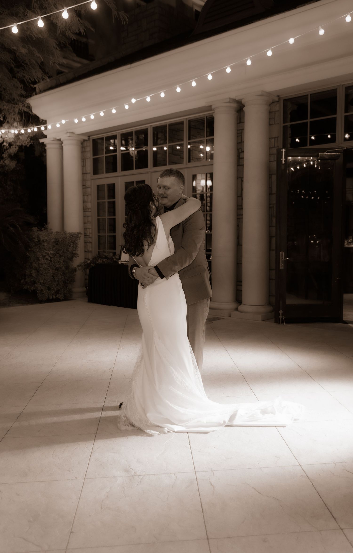 Intimate slow dance moment between newlyweds under twinkling lights and columns.