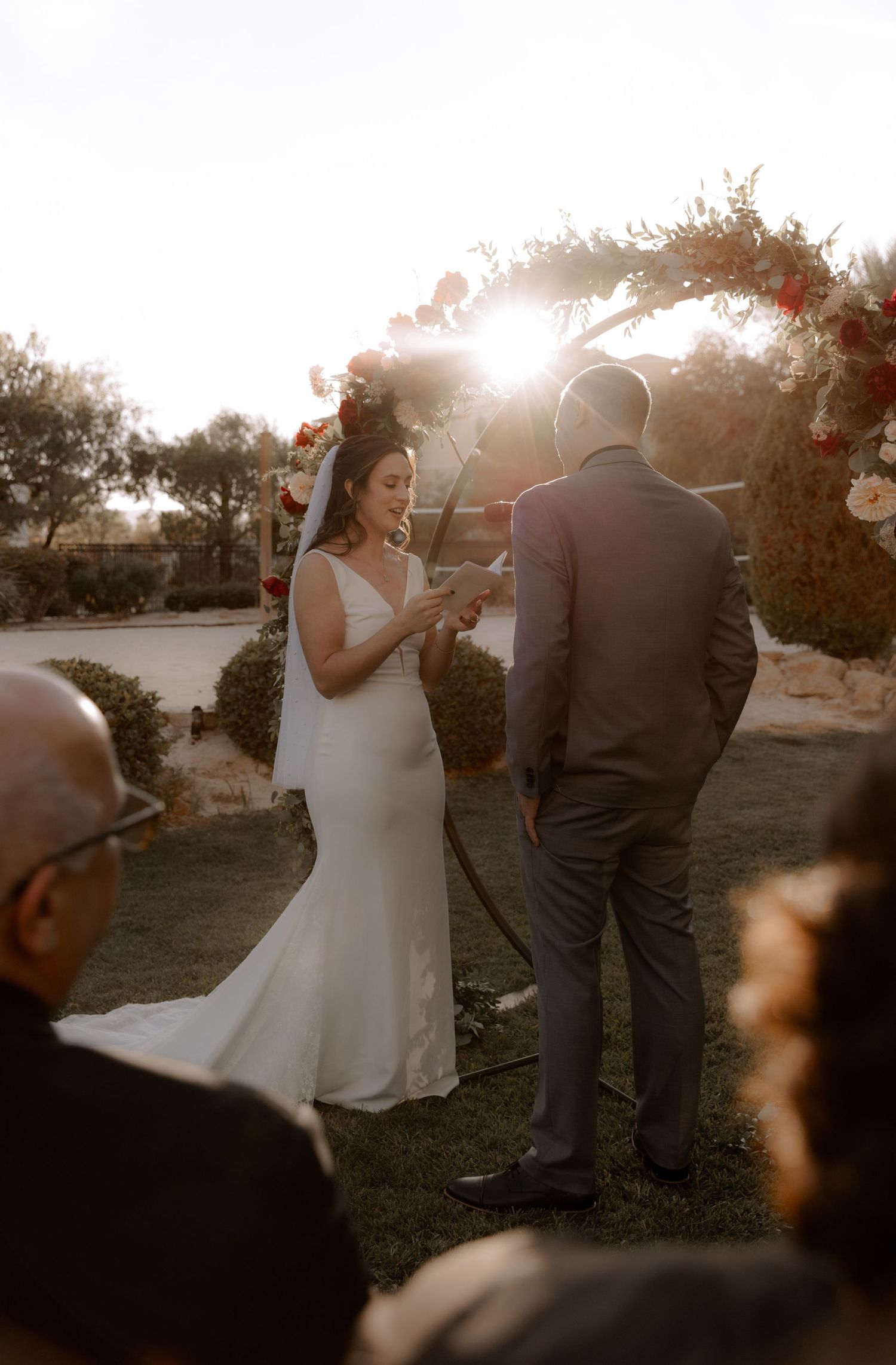 A wedding ceremony under a floral arch with golden sunlight streaming through.