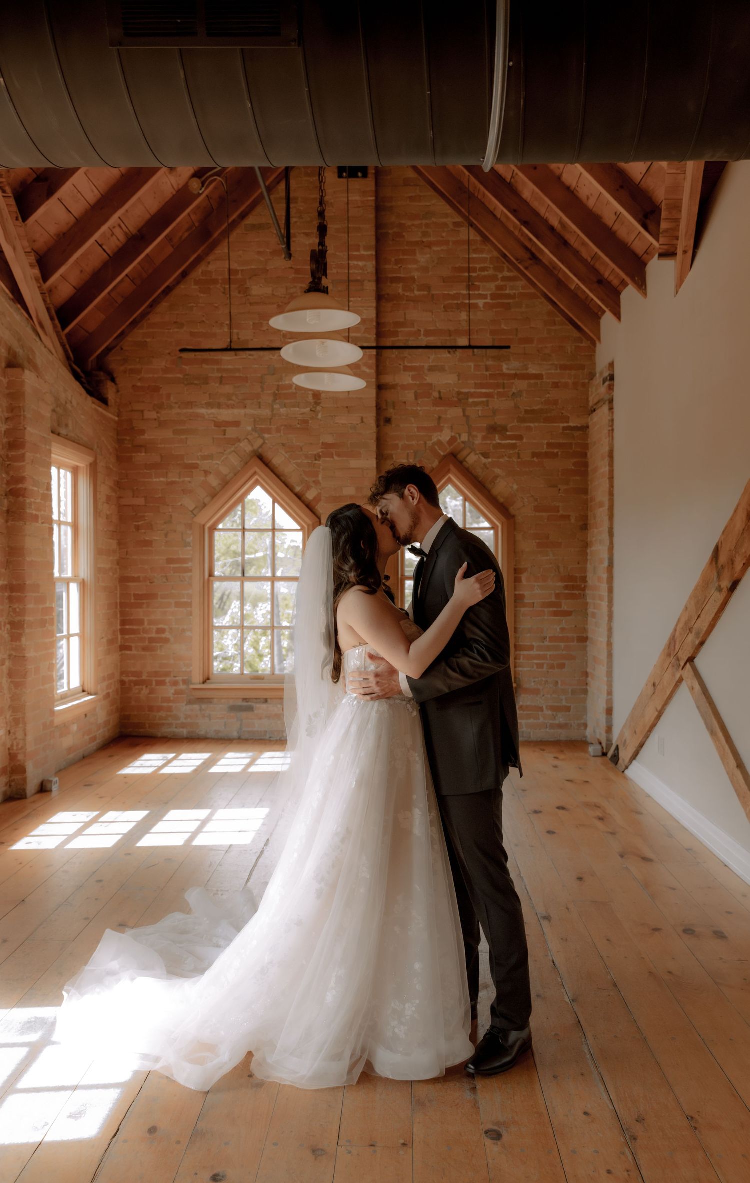 Intimate wedding moment in rustic chapel with exposed wooden beams and natural light.