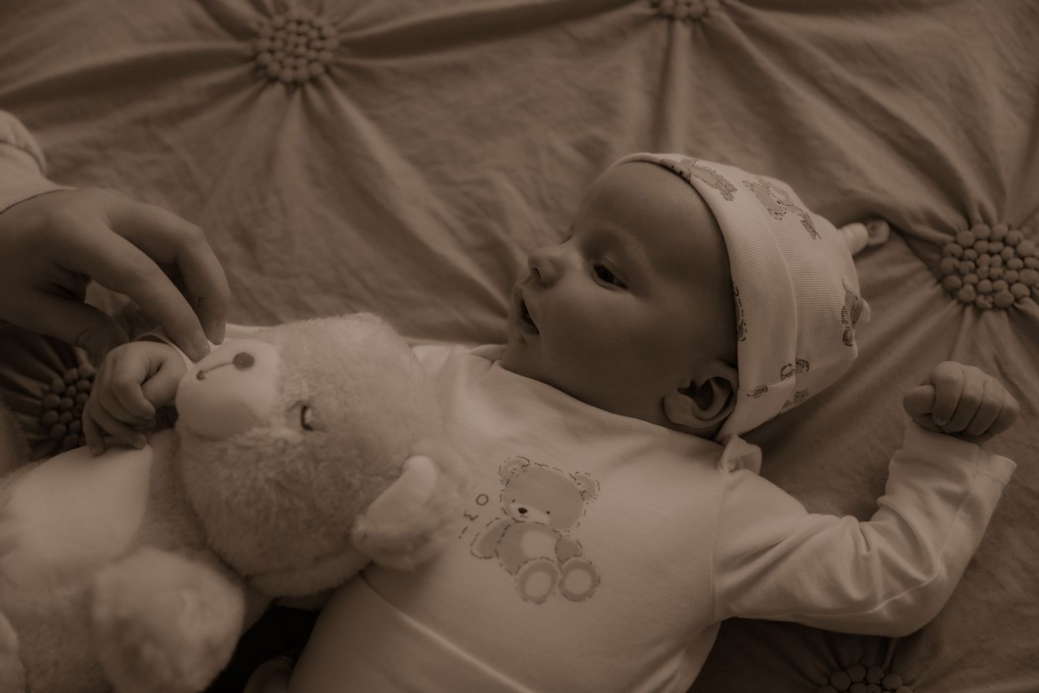 A baby rests peacefully on a textured blanket while wearing light-colored clothing and a head covering.