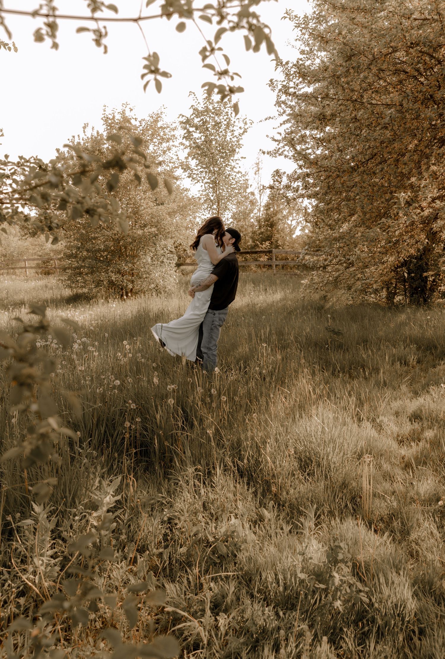 Couple embraces in a sepia-toned meadow surrounded by tall grass and autumn trees.