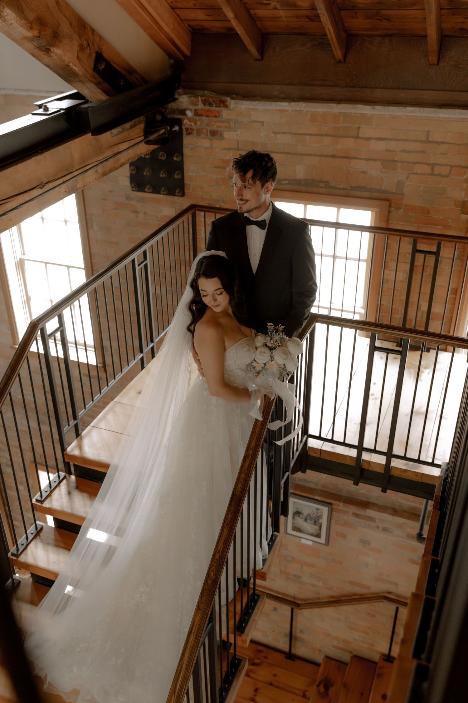 Wedding couple posing on an industrial staircase with exposed brick walls and wooden beams.