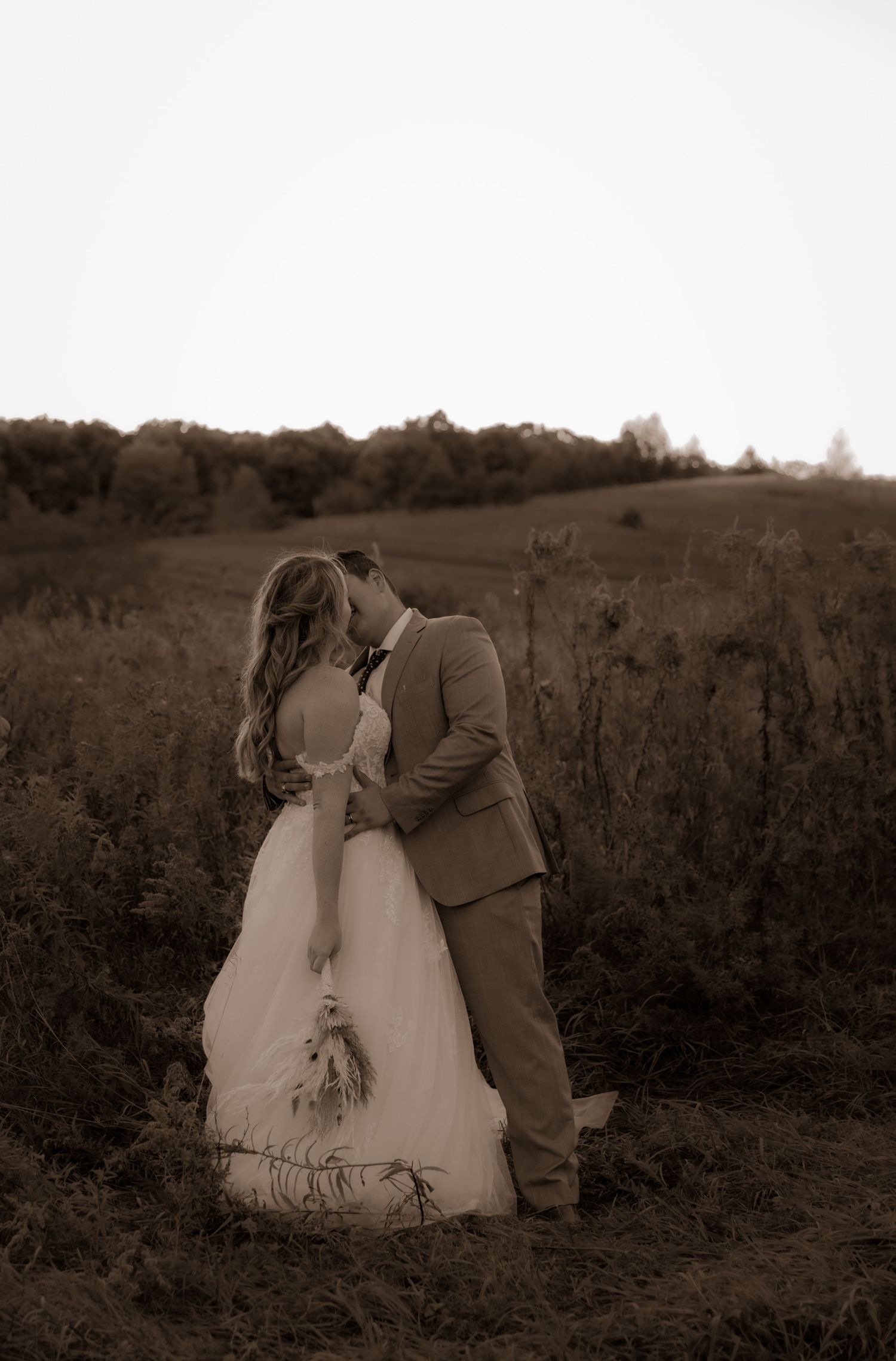 Intimate wedding couple moment captured in sepia tones against natural landscape.