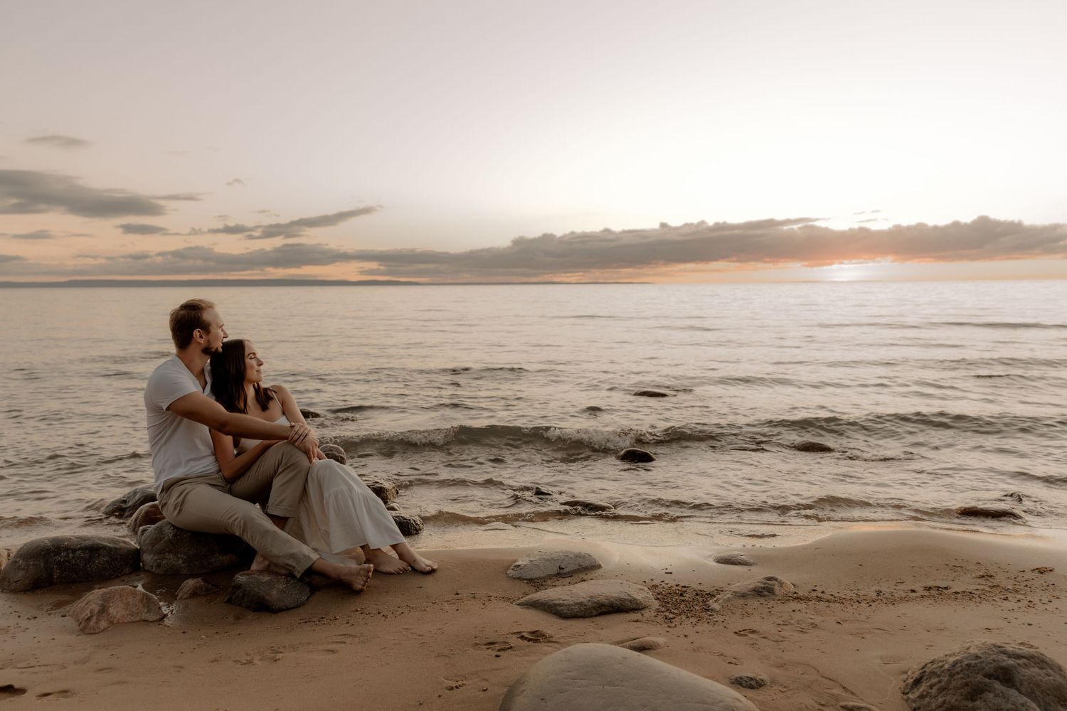 Couple watching sunset together while sitting on rocky beach by ocean.