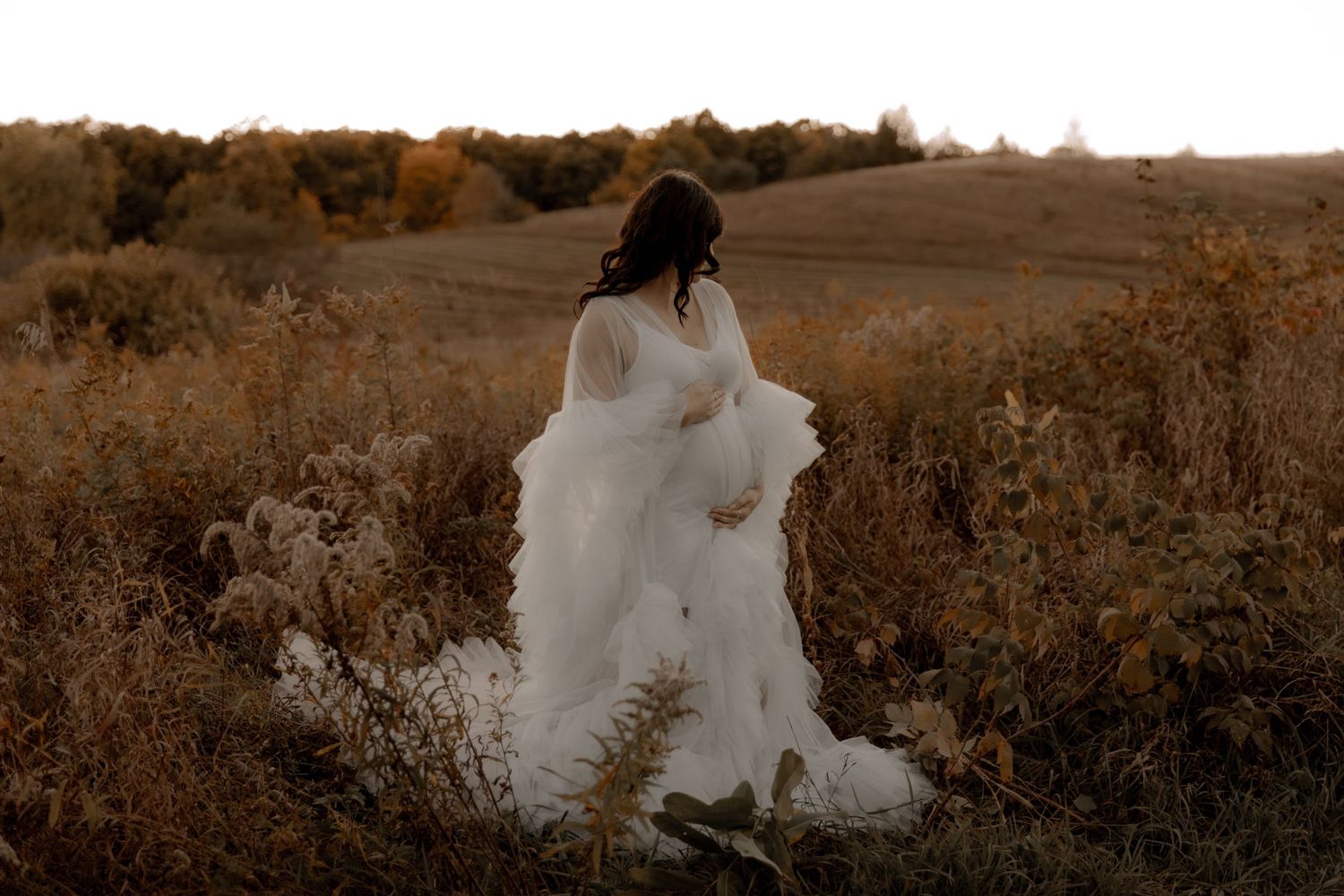 A romantic maternity photo captured during golden hour in a rustic autumn field.