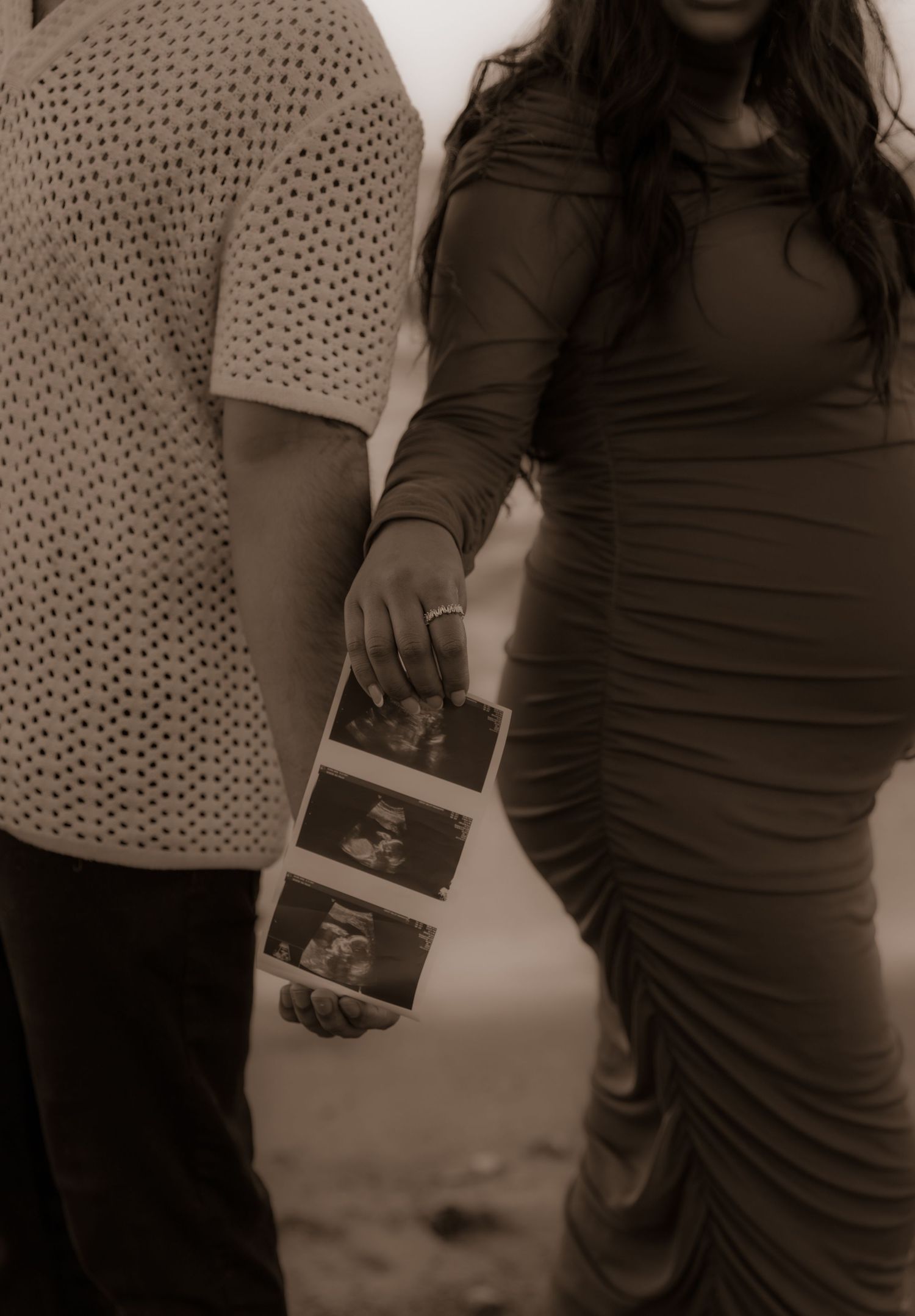 A sepia-toned photo shows a couple holding ultrasound images during a pregnancy announcement photoshoot.