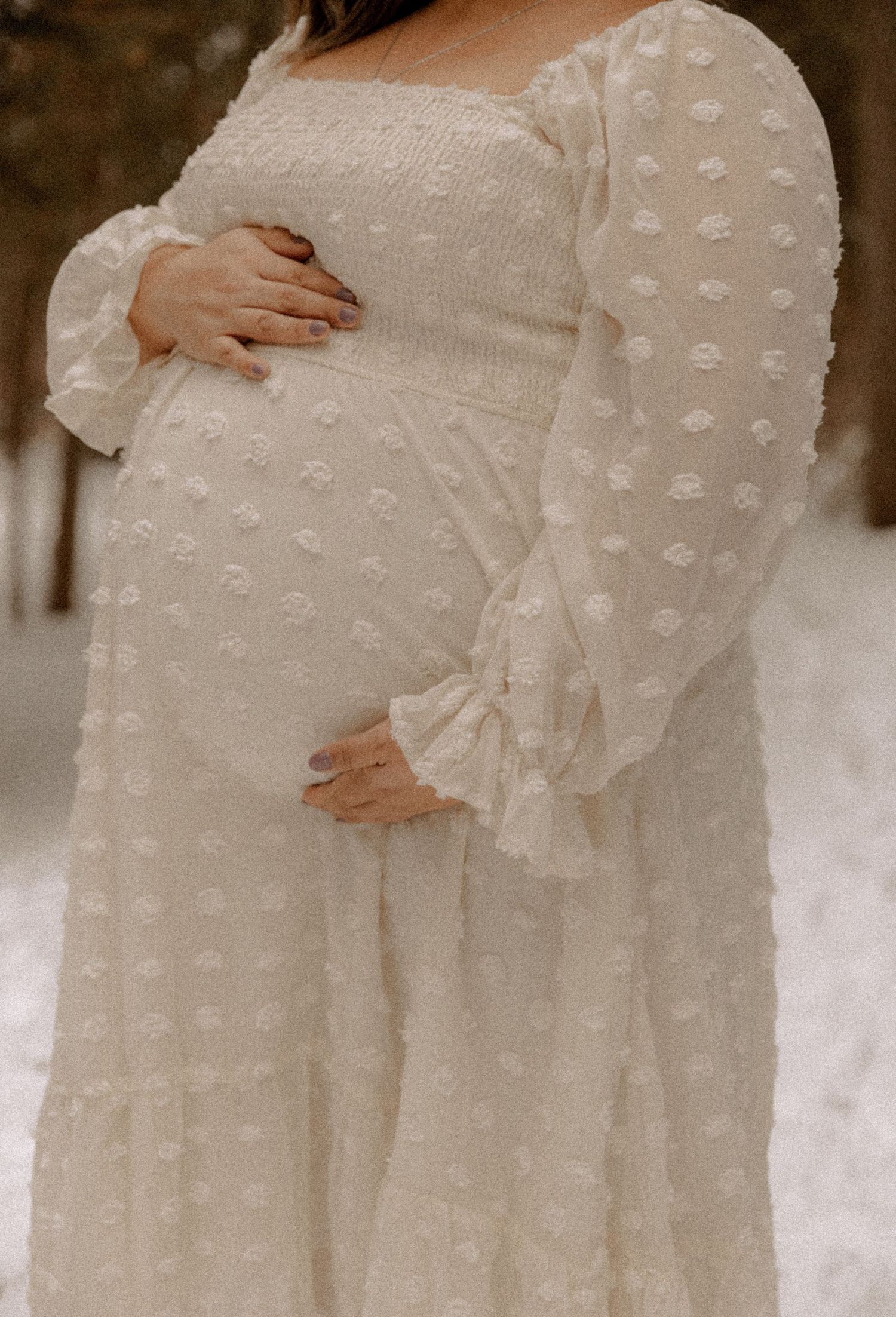 A delicate white maternity dress with textured polka dots and romantic ruffle sleeves frames a growing baby bump.